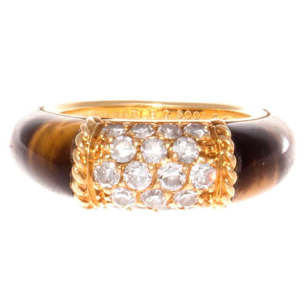 The classic Philippine ring from Van Cleef & Arpels. Designed with pave set diamonds in textured 18k yellow gold accented by vibrant multihued tiger's eye cascading down either side. Signed VCA, numbered and stamped with French hallmarks. 

Ring