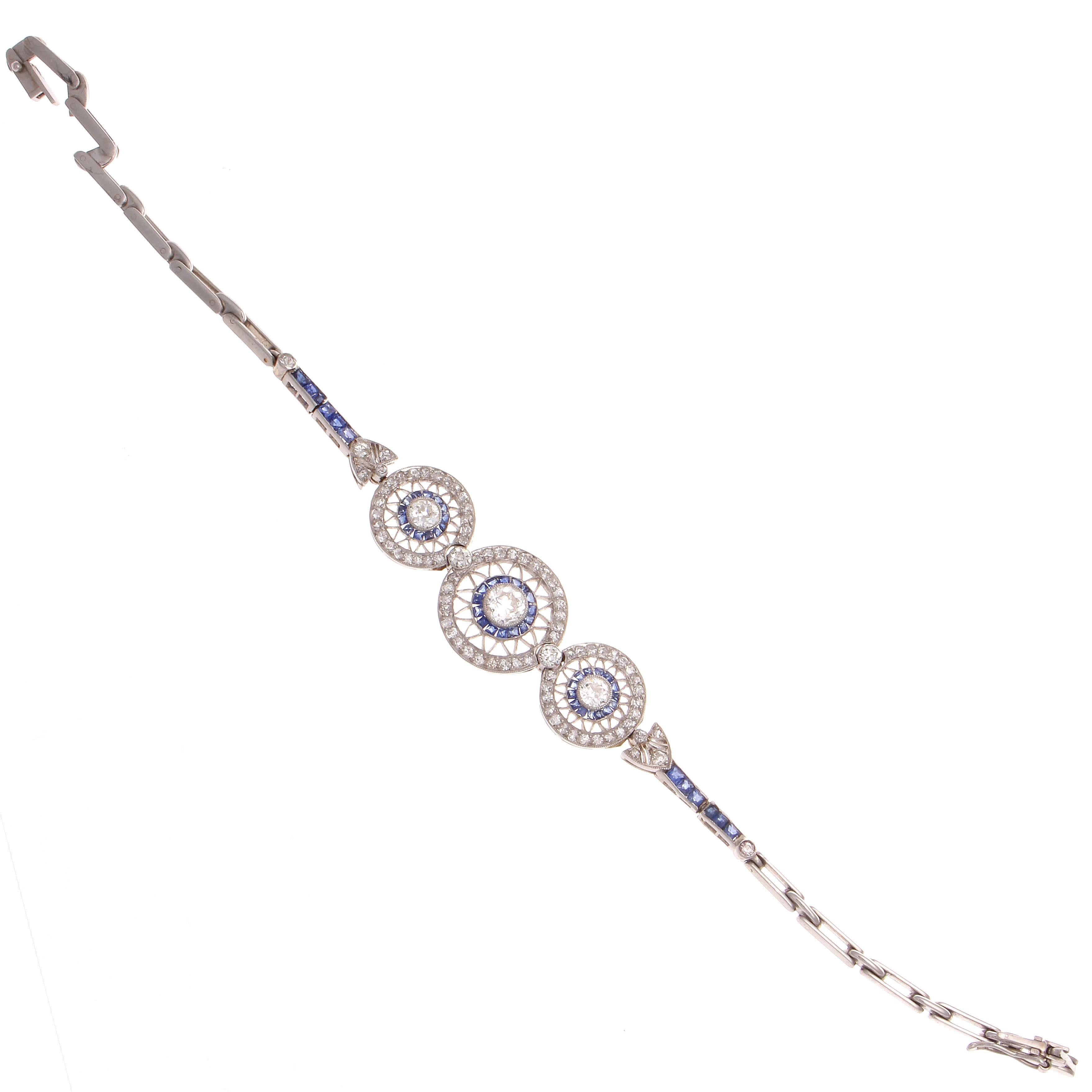 The allure of the Art Deco time period has inspired the creation of this exceptional bracelet. Featuring a 0.50 carat old European cut diamond surrounded by a halo of vivid blue sapphires and a halo of perfectly matching white diamonds separated by