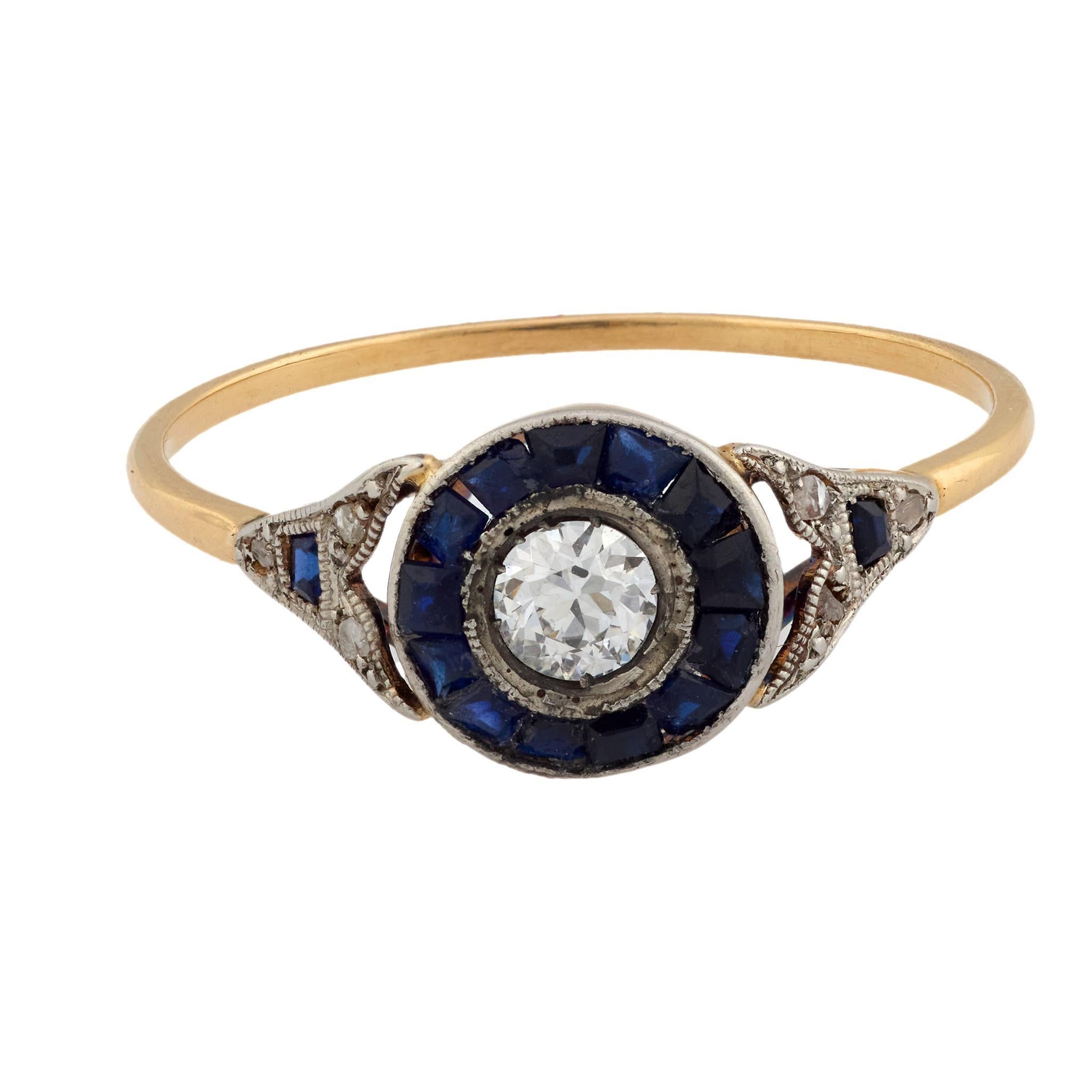 Cette bague Art déco des années 1930 présente en son centre un diamant de taille européenne ancienne de 0,20 carat, d'une couleur G-H et d'une pureté VS2. Encadré par quinze saphirs bleus profonds taillés en calibre totalisant environ 0,30 carat,