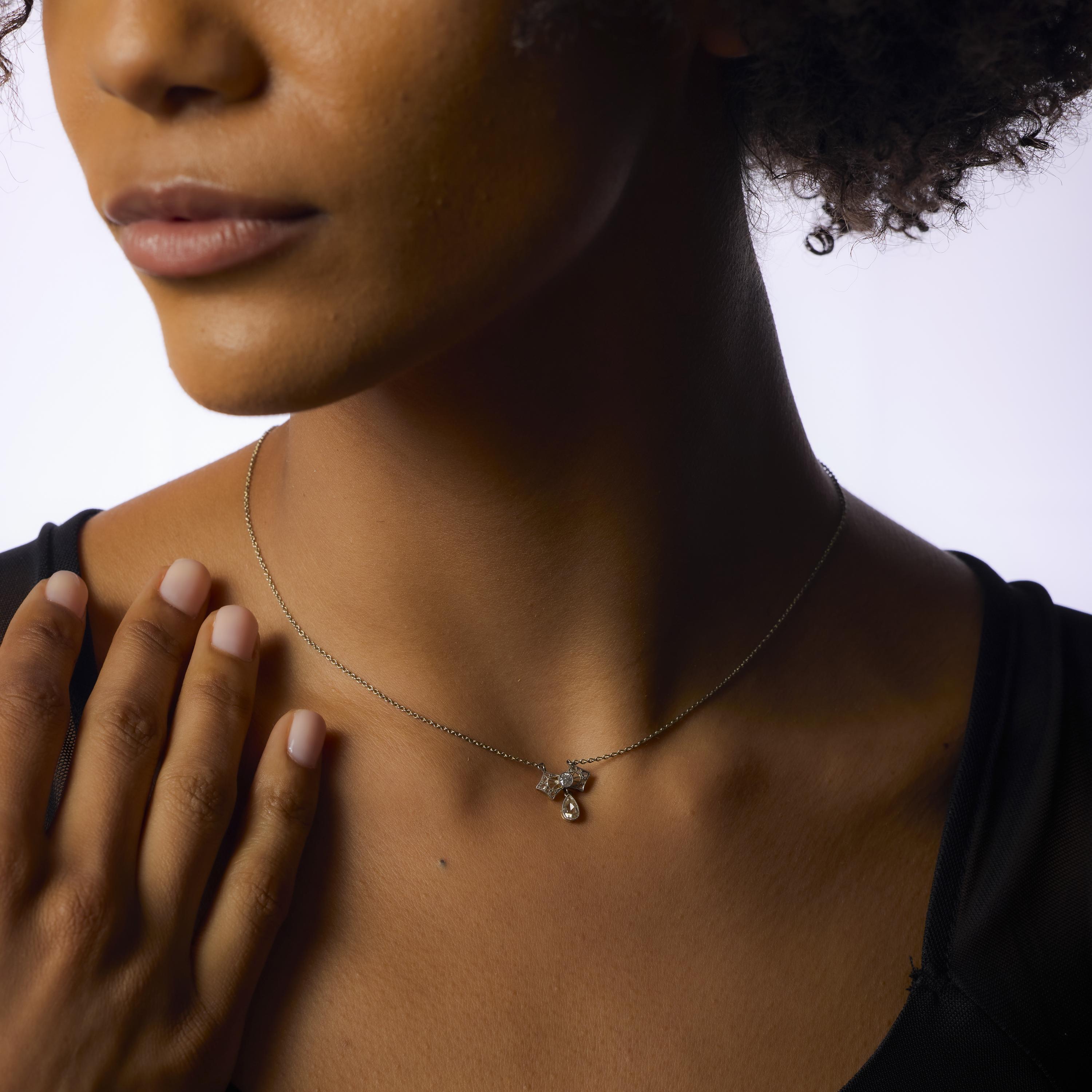 Ce délicat collier victorien du début des années 1900 met en valeur un diamant poire ancien d'environ 0,25 carat en son centre, qui brille doucement d'une couleur M-N et d'un charme antique. Autour d'elle, onze diamants ancienne mine et taille rose