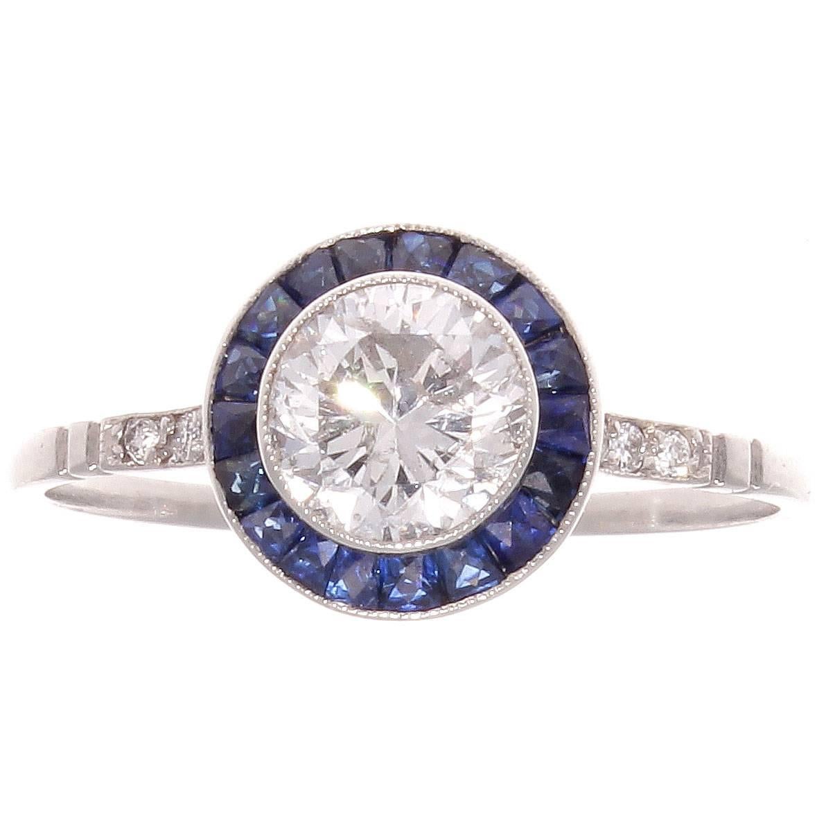 The glamorous era of the art deco period have influenced designers to recreate the jewelry from this remarkable time. Featuring a 0.80 carat diamond that is H color, SI2 clarity surrounded by a halo of navy blue sapphires. Crafted in platinum.