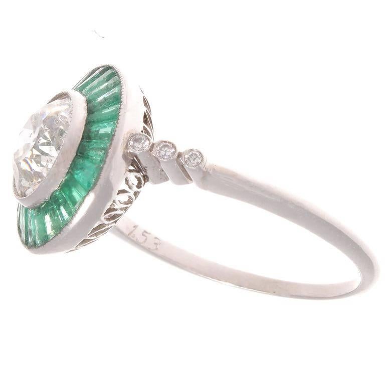 The well proportioned 1.53 old European cut diamond is I color and SI2 clarity. The diamond is completely surrounded by 27 forest green emeralds. The contrast of color emphasizes the diamond's sparkle. The hand made platinum ring features a basket