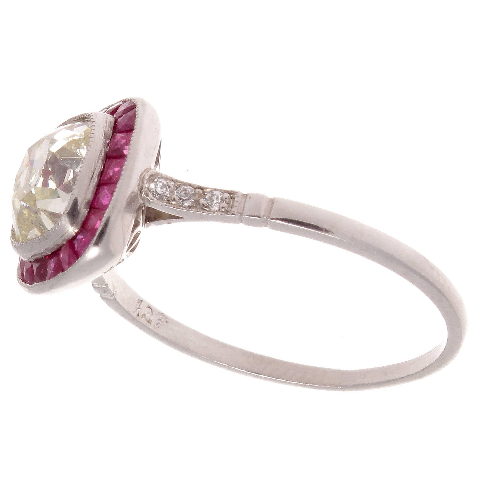 Style from the golden art deco era of jewelry has inspired this unique rendition of the traditional engagement ring. Featuring a 1.27 carat old cushion cut diamond that is surrounded by an untraditional halo of vibrant red rubies making the diamond