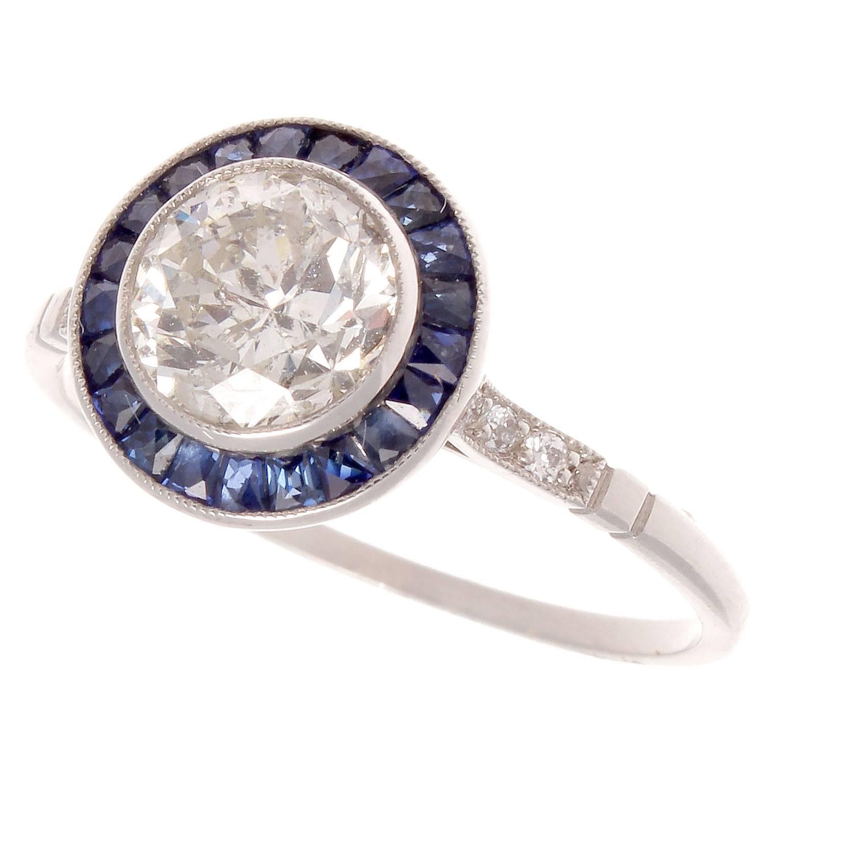 The 1930's is regarded as the golden era of jewelry and has influenced designers to recreate the jewelry from this remarkable time. Featuring a 1.15 carat diamond that is surrounded by a halo of navy blue sapphires. Crafted in platinum. 
