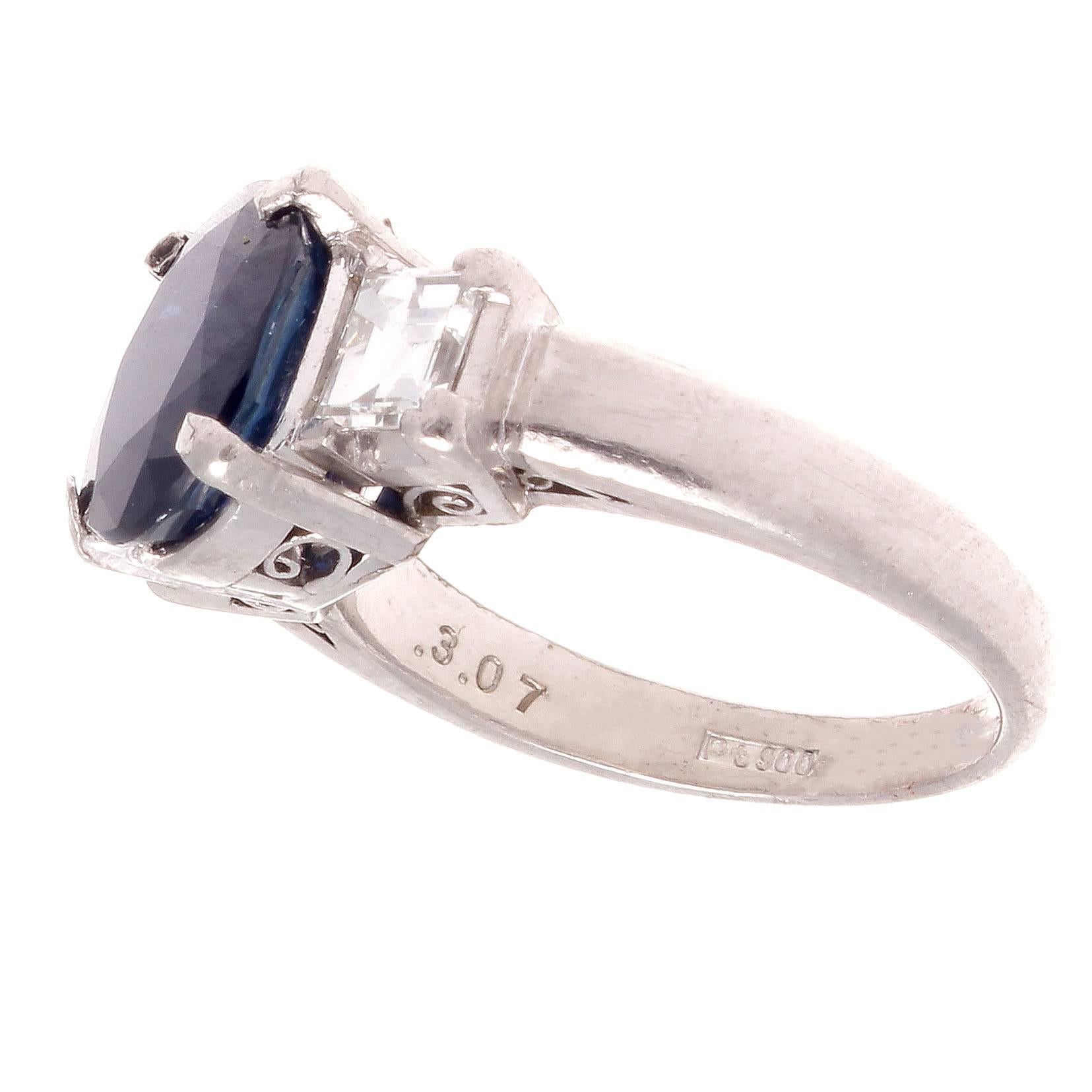 A new modern take on the classic engagement ring that is becoming ever popular in the new generation. Featuring a 3.07 carat vivid navy blue sapphire accented on either side by two near colorless emerald cut diamonds. Crafted in platinum.

Ring size