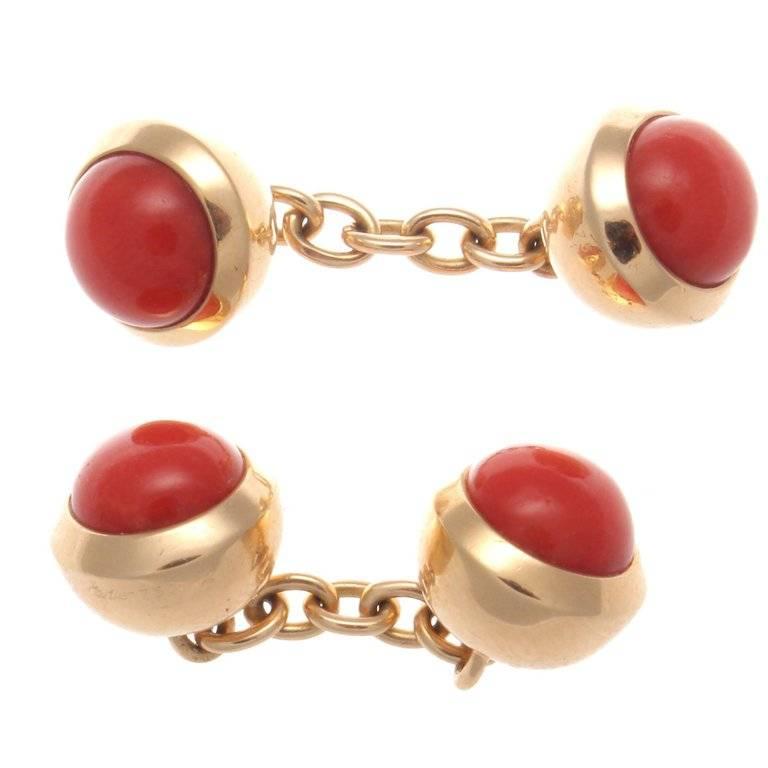Elegance and pure design is innate in all of Cartier's creations. Featuring bright cabochon cut reddish orange coral bezel set in 18k glistening yellow gold balls. Signed Cartier.