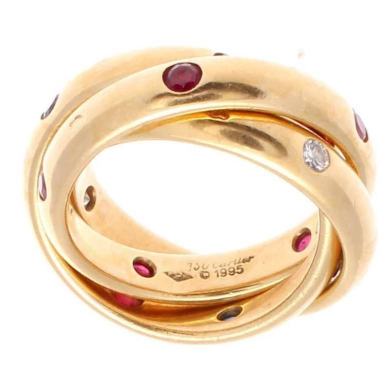 Cartier, elegant and timeless. A modern rendition of the trinity ring that has been part of the Cartier family since 1924. Designed with lively rubies, sapphires and diamonds. Crafted in 18k yellow gold.   

Ring size 4 3/4.