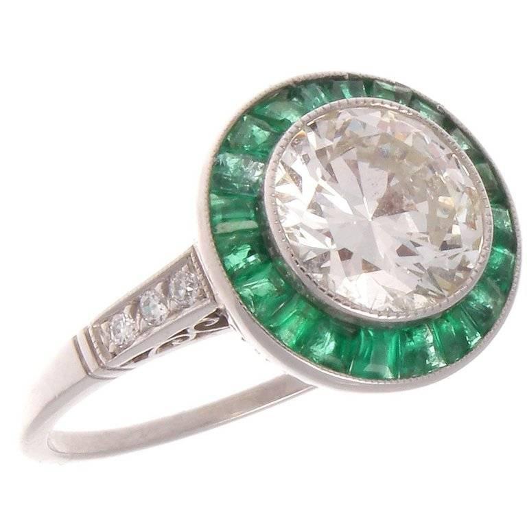 A timeless design that starts its beginnings in the later part of the 19th century. Featuring a 1.80 carat round brilliant cut diamond that is J-K color, VS1 clarity. Surrounded by a vibrant halo of forrest green emeralds. Hand crafted in