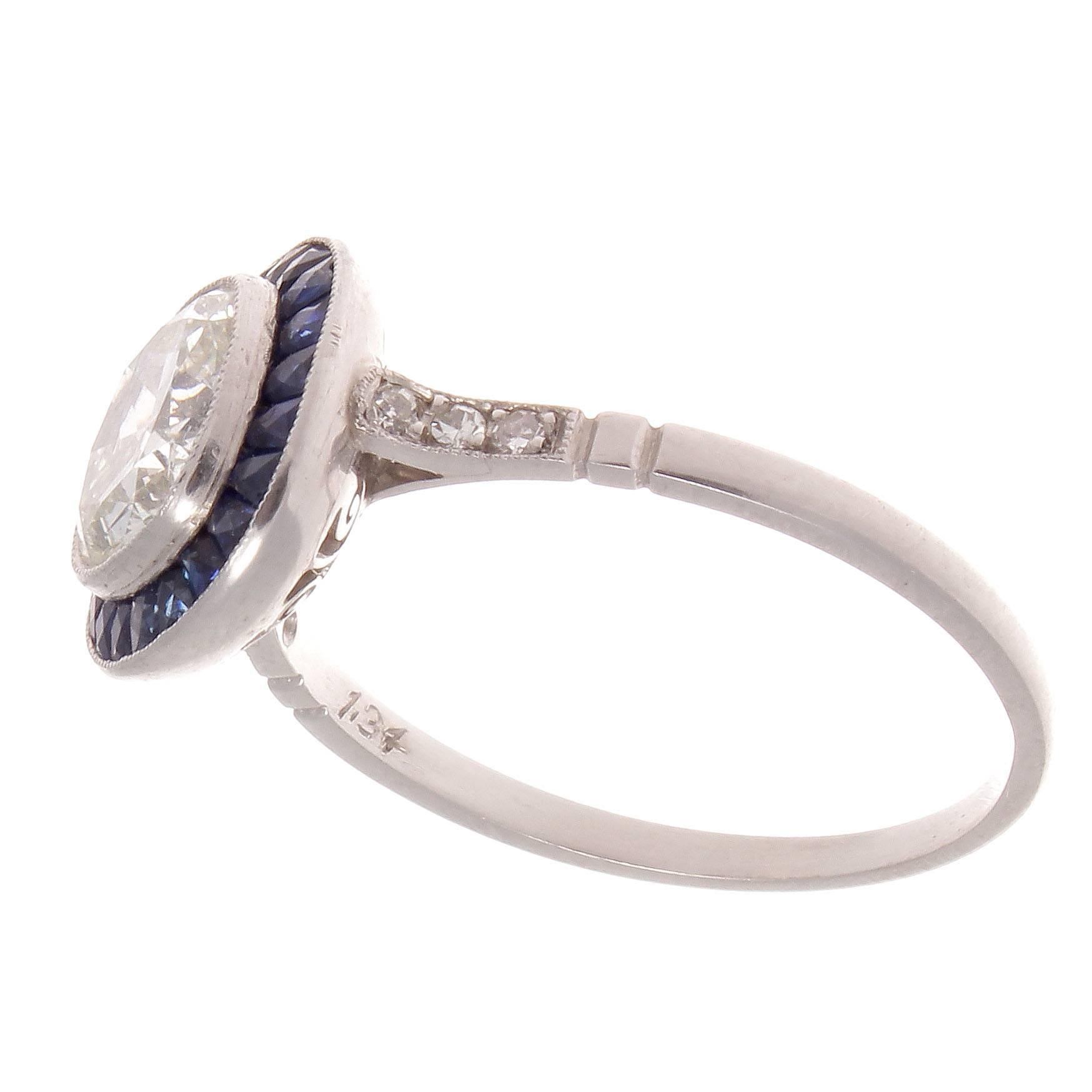 The glamorous art deco period has heavy influences on this fusion of classic and nontraditional engagement rings. Featuring a 1.34 carat diamond that is surrounded by a halo of navy blue sapphires. Crafted in platinum. 

Ring size 6 and may be