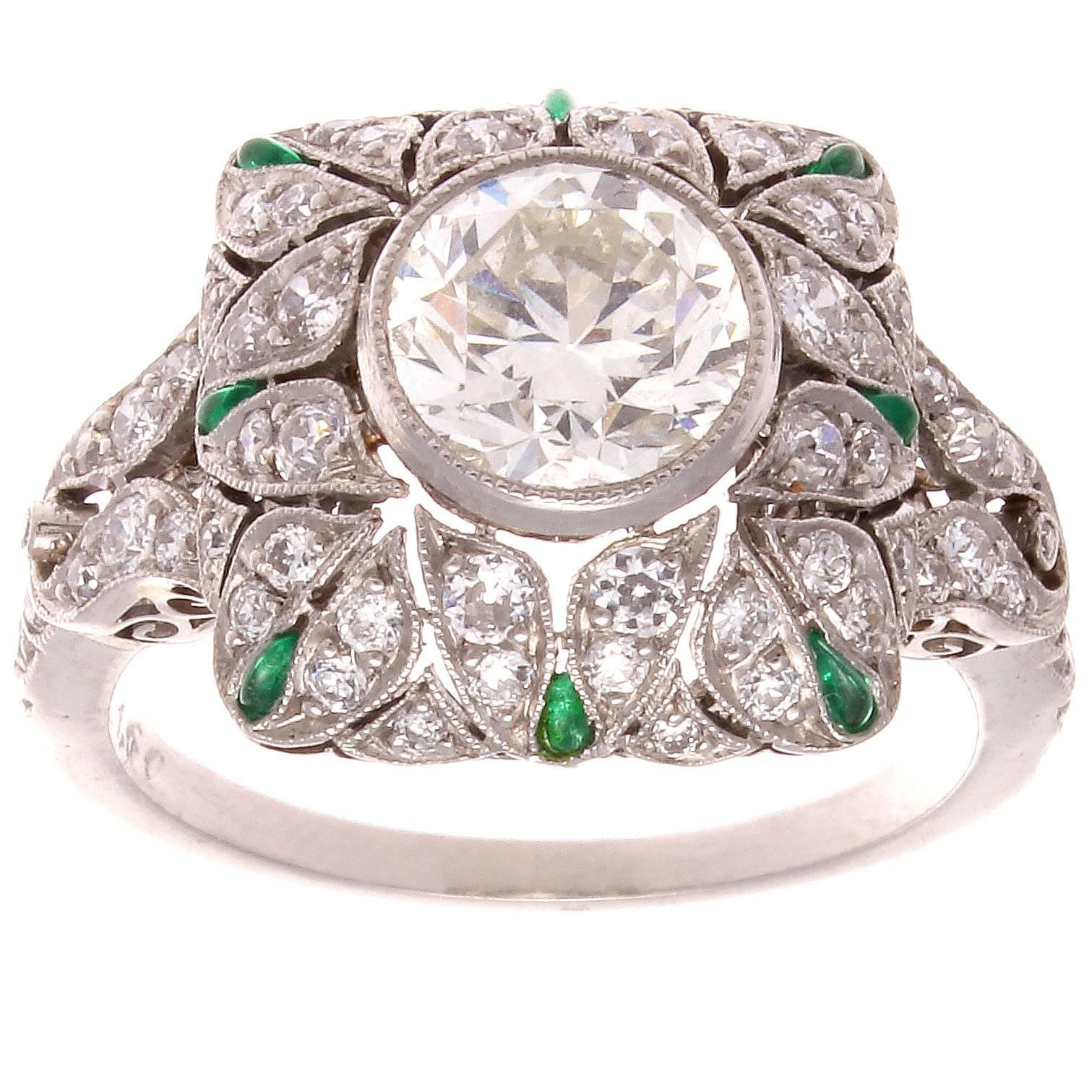 The allure of the Art Deco time period has inspired the creation of this exceptional engagement ring. Featuring a 1.60 carat center diamond that is H color, VS clarity and is surrounded by near colorless diamonds and vibrant green emeralds. Expertly