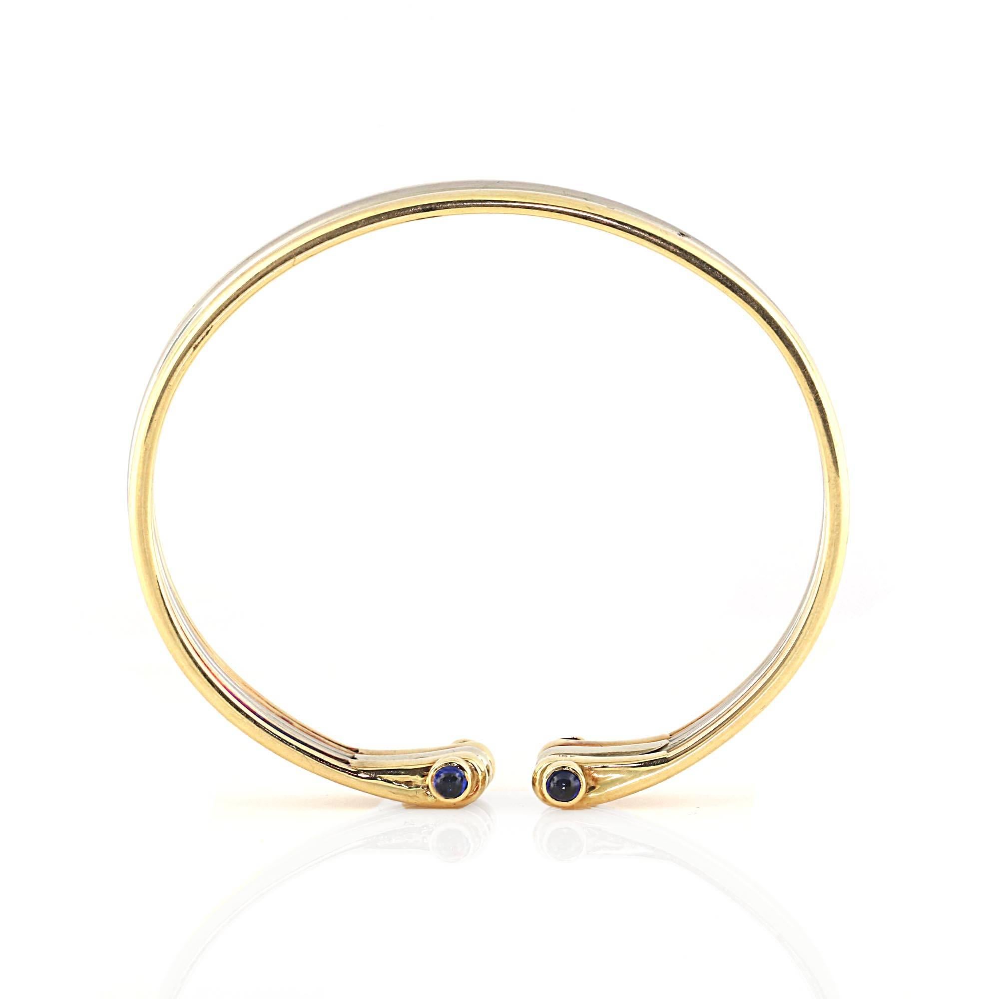 Truly a classic bracelet. A white gold band wrapped between two yellow gold bands. Each side of the bracelet contains 2 cabochon (rounded) sapphires white are bezel set. The bracelet has an opening in the center for easy placement on the wrist.