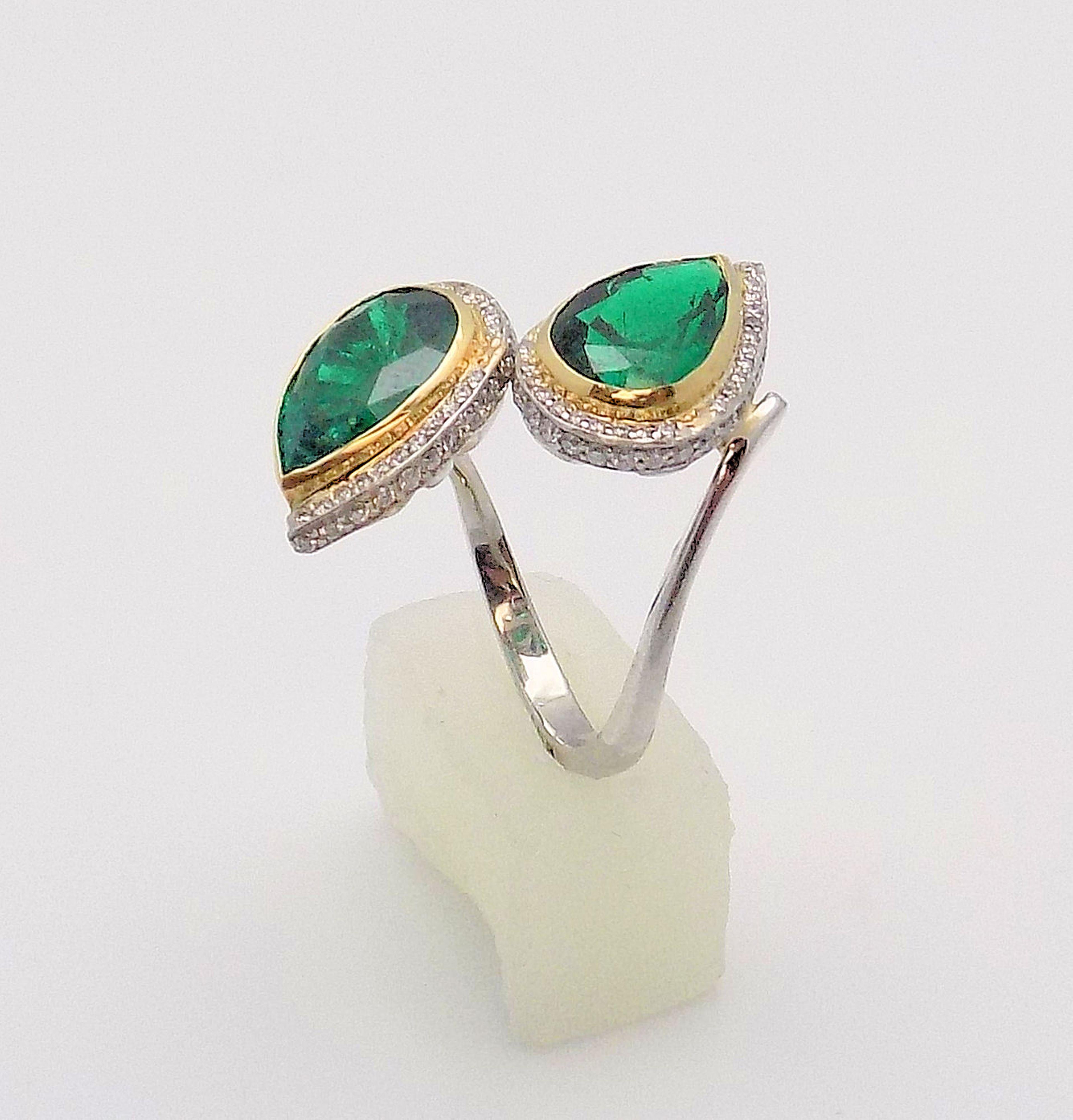 Dramatic Platinum and 18 karat Yellow Gold Ring of Matching Pear Shaped Emeralds Surrounded by Diamonds. Emeralds 2.10 Carat and 2.13 Carat; 84 Round Brilliant Diamonds 0.25 Carat Total Weight, VS, H-I; Finger Size 6.5; 5.6 DWT or 8.71 Grams.