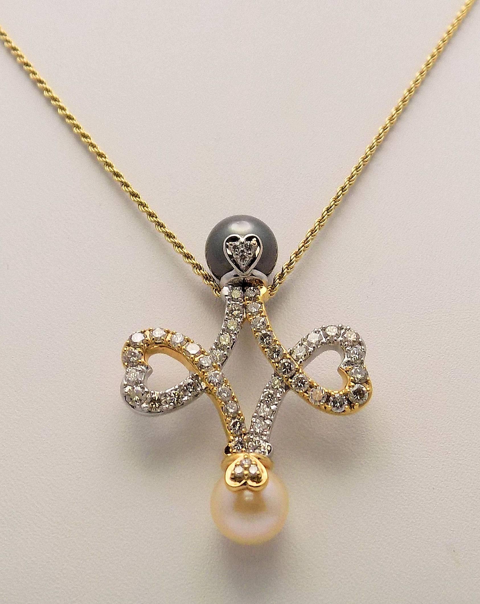 Double heart pendant in 18 Karat yellow and white gold set with diamonds and black and white South Sea Pearls.  The black pearl measures 10 mm. and the white pearl measures 9.5 mm.  Also 48 round diamonds 1.30 carat total weight VVS-2, H.  Attached
