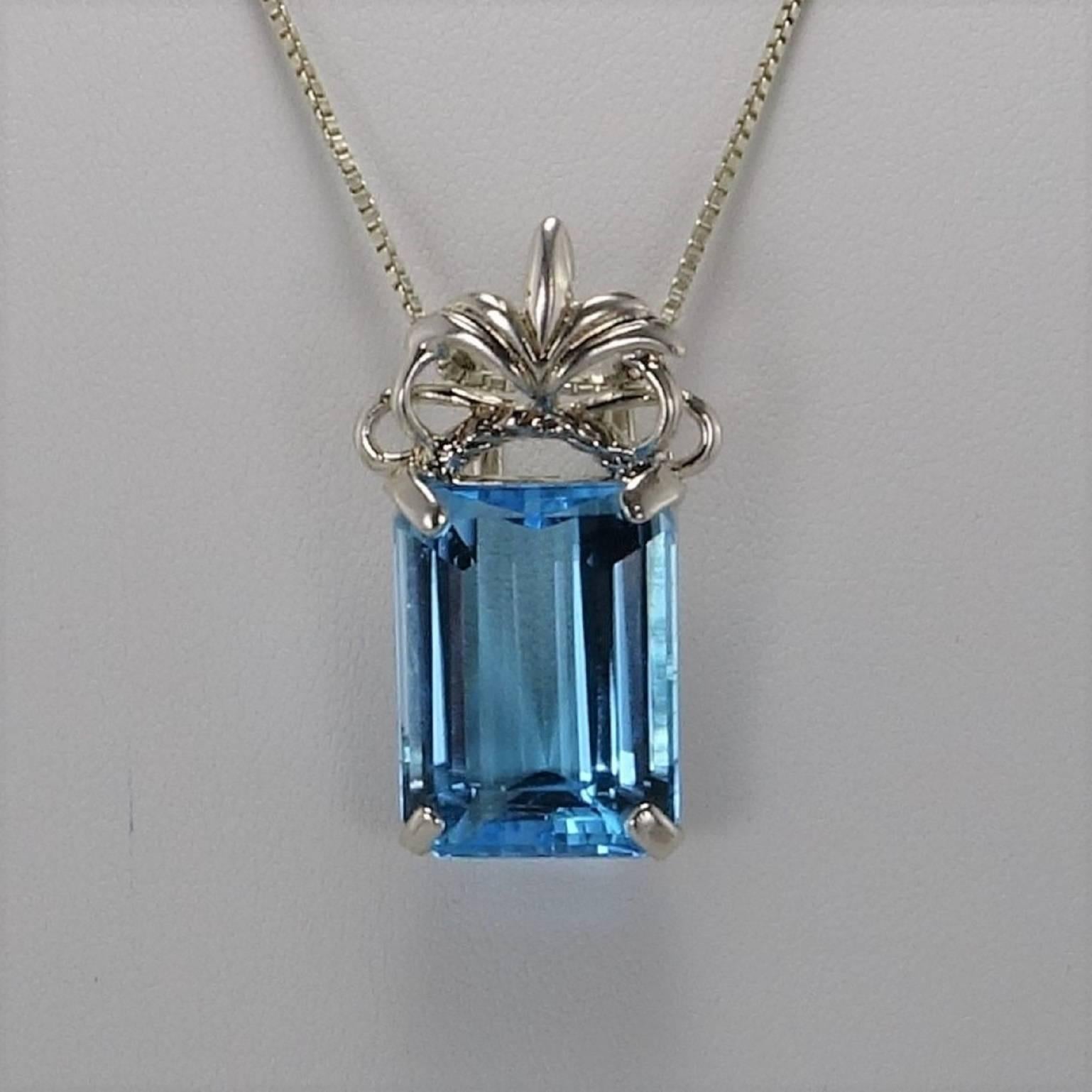 Sparkling Sky Blue Topaz of 26.95 carats set in a Pendant of ornate Sterling Silver. This Blue Topaz is Emerald Cut and brillant. The Emerald Cut is an interesting contrast to the Scrolly Crest atop the gemstone. The overall length is 1 3/8 inches.