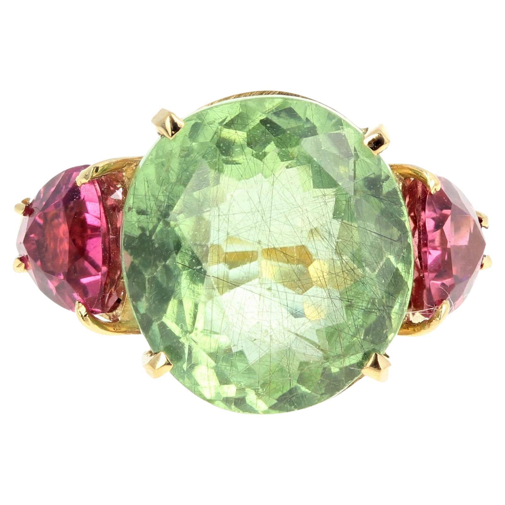 Unique 6 carat sparkling oval green Tourmaline (13 mm x 11.7 mm) enhanced with two glittering pink trillion cut Tourmalines (6 mm x 6 mm approximately) set in an 18 Kt yellow gold handmade ring size 5 (sizable). There are no eye visible inclusions