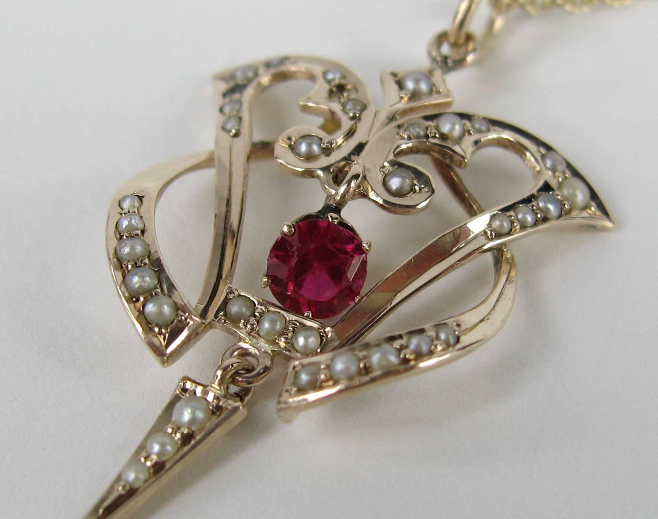 This is breathtaking, antique 10k Gold Lavaliere with prong-set Ruby. An intricate design that intertwines. Delicate seed pearls set. Dangling Seed pearl at the bottom. Measuring 1.65 in x .84 in. Attached is a 14K gold Chain measuring 18.5 in end