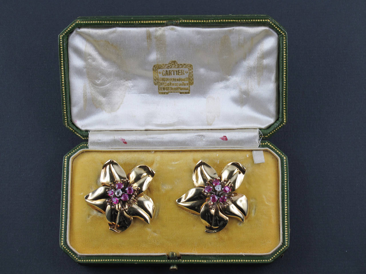 A pair of Cartier London yellow gold, diamond and ruby clips brooches. 
Of flower design, In original fitted Case. One brooch signed and numbered. 
1940's