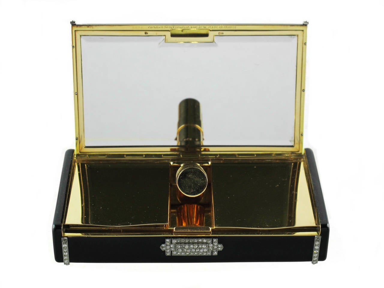 A Cartier yellow gold and platinum enamel vanity case. 
The black enamel case decorated with two lines of millegrain-set rose and emerald-cut diamonds, enhanced with palmette motifs and diamond thumbpiece, opening to reveal  a mirror, a lipstick