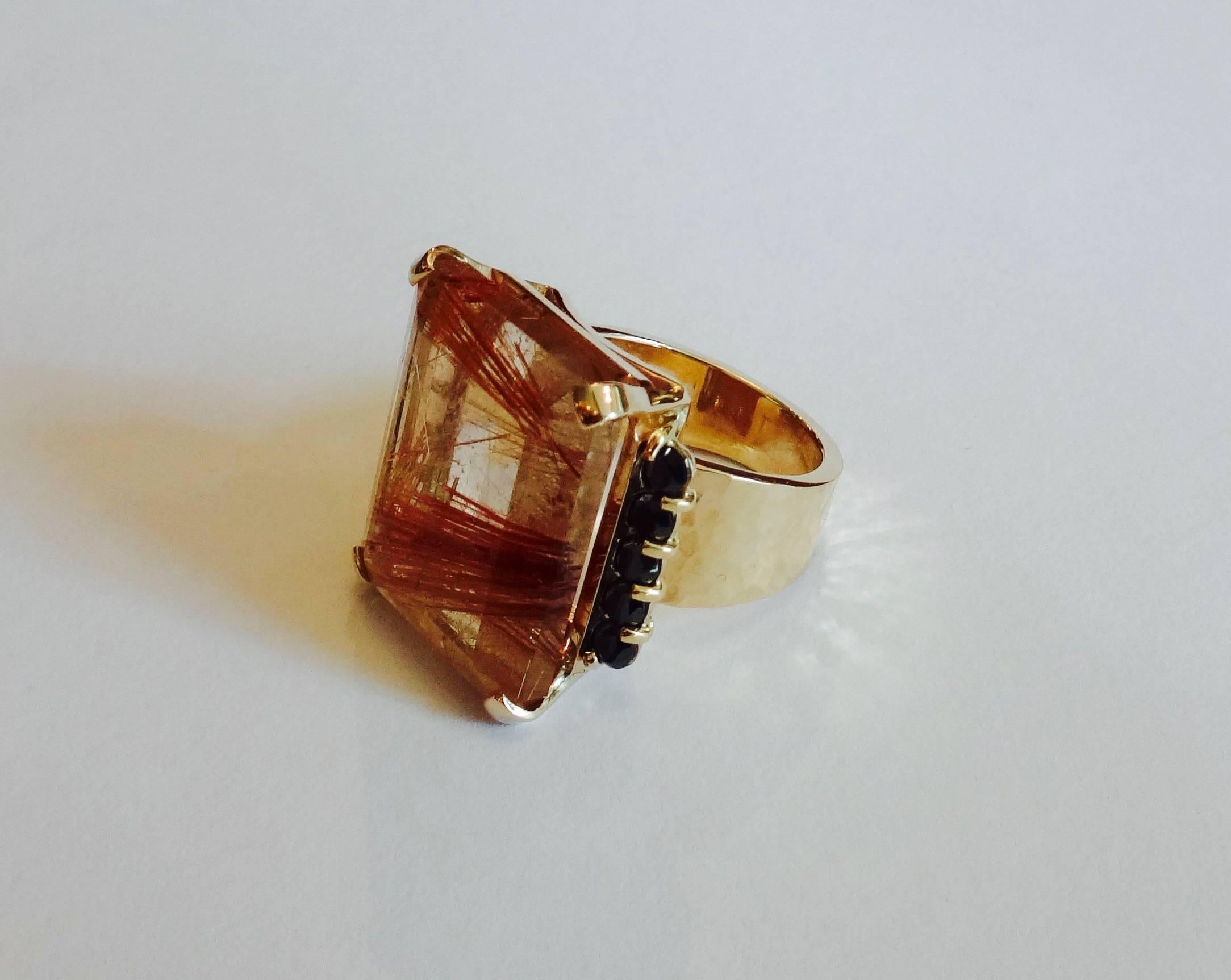A dramatic copper colored, 53.77 carat rutilated quartz (needles of titanium dioxide trapped within clear quartz, origin: Brazil) is flanked by eight, brilliant cut black diamonds all set within a hand fabricated 18k hammered gold setting.  The ring