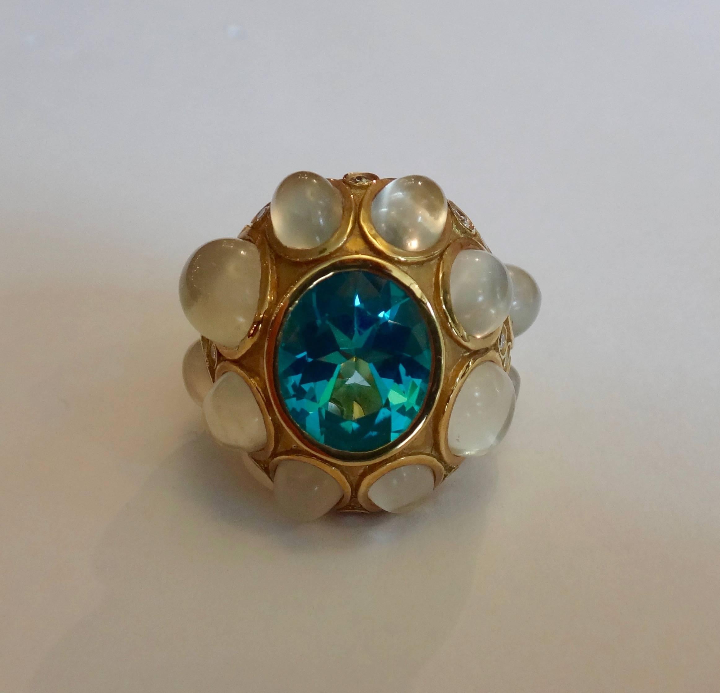 Bright blue topaz (5.79 carats) is paired with a rare collection of white cat's eye moonstones of various sizes (12 at 13.74 carats) and bezel set diamonds (14 at .42 carats).  All set in a textured 18k yellow gold dome ring containing beautiful