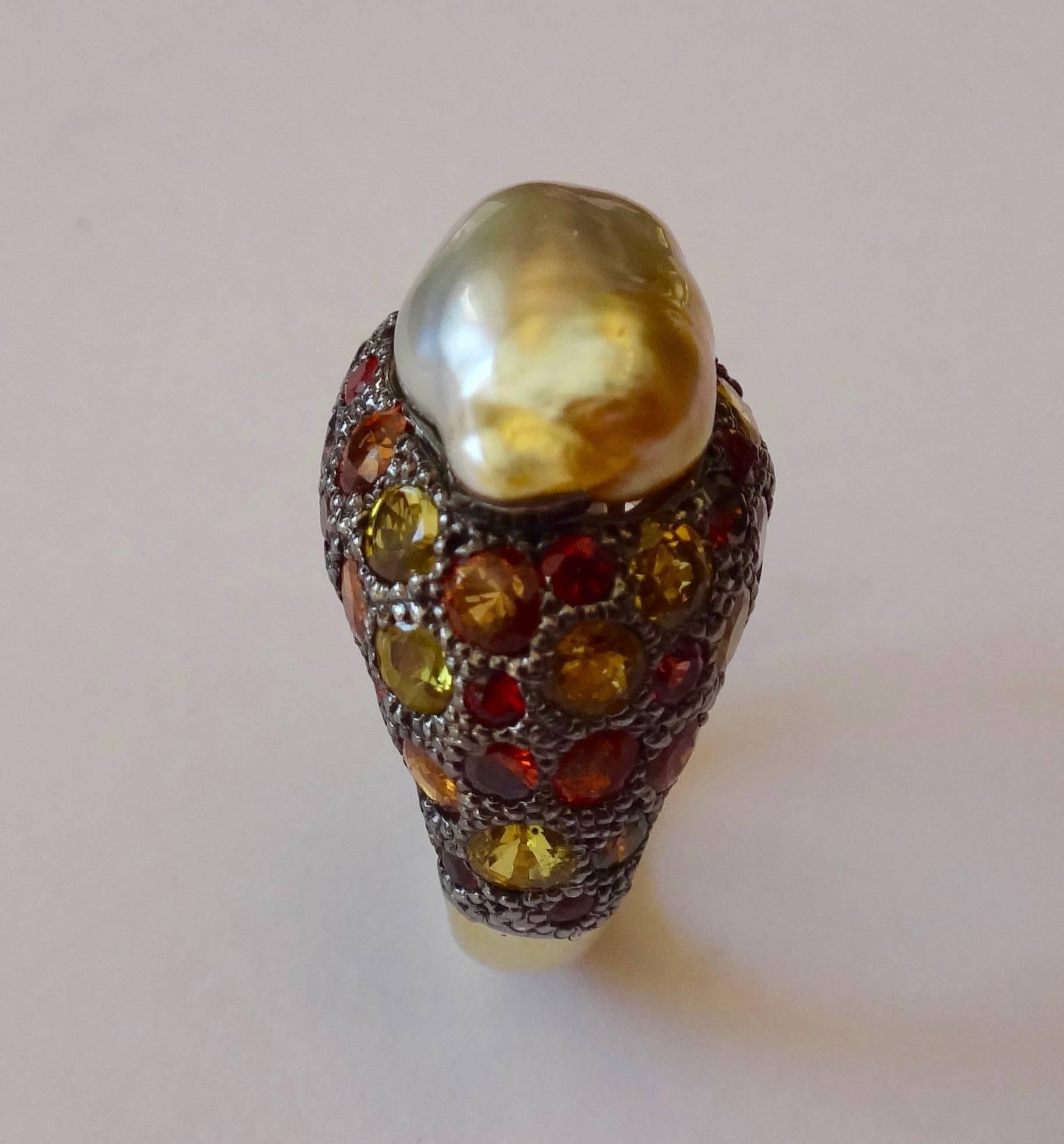 A Maluka pearl (Origin: Indonesia) in shades of gray and gold is mounted in a pave set dome ring of yellow and orange sapphires along with cognac colored diamonds.  The pave work is executed in blackened silver.  The remainder of the ring, including