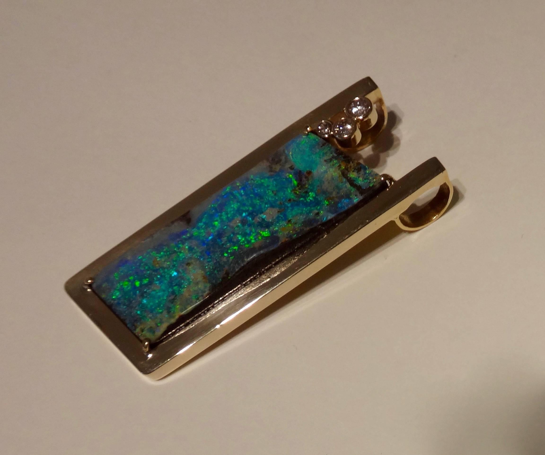 A trapazoid shaped, very sculptural Boulder Opal in shades of aqua, lime green and royal blue is decorated with three bezel set diamonds.  All are set in a handmade and one-of-a-kind 18k yellow gold mount.  (The slide/pendant is shown on a silk cord
