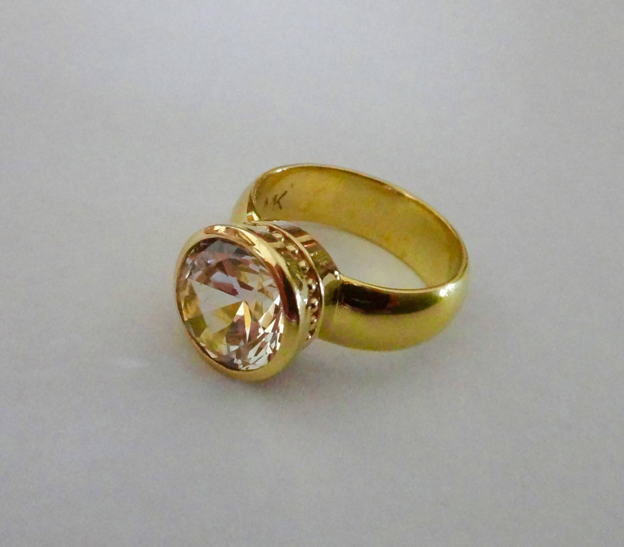 A 10mm round cut white sapphire is bezel set in an 18k yellow gold "Leah" ring.  Beaded detail around the bezel adds interest.  The ring looks beautiful alone or may be stacked with other Michael K. Jewels "Leah" rings for some