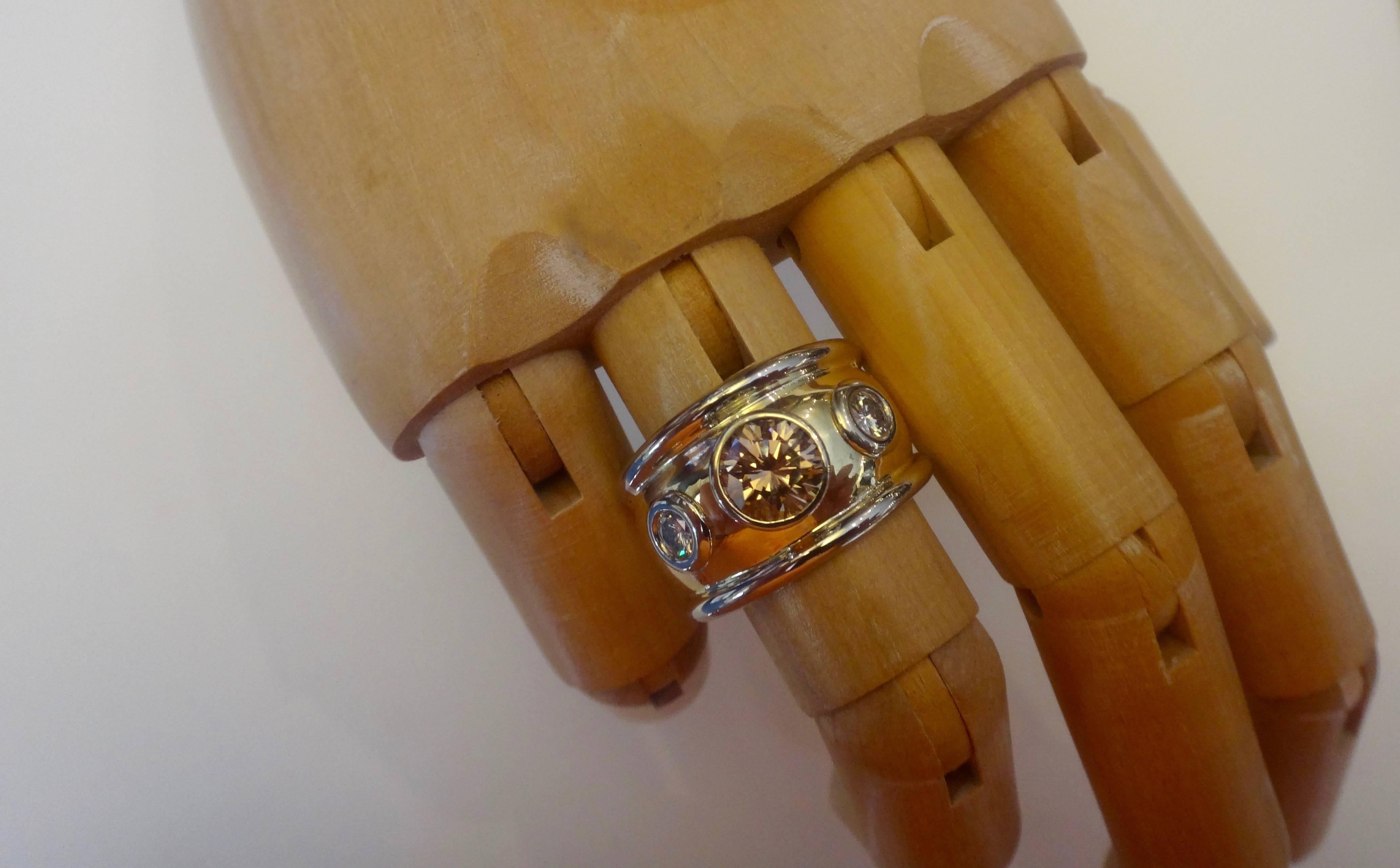 A brilliant cut cognac colored diamond is enhanced with a pair of brilliant cut white diamonds in this Bombe style ring.  The mounting is hand fabricated. The body of the ring is 18k yellow gold.  The gems are bezel set in white gold as are the