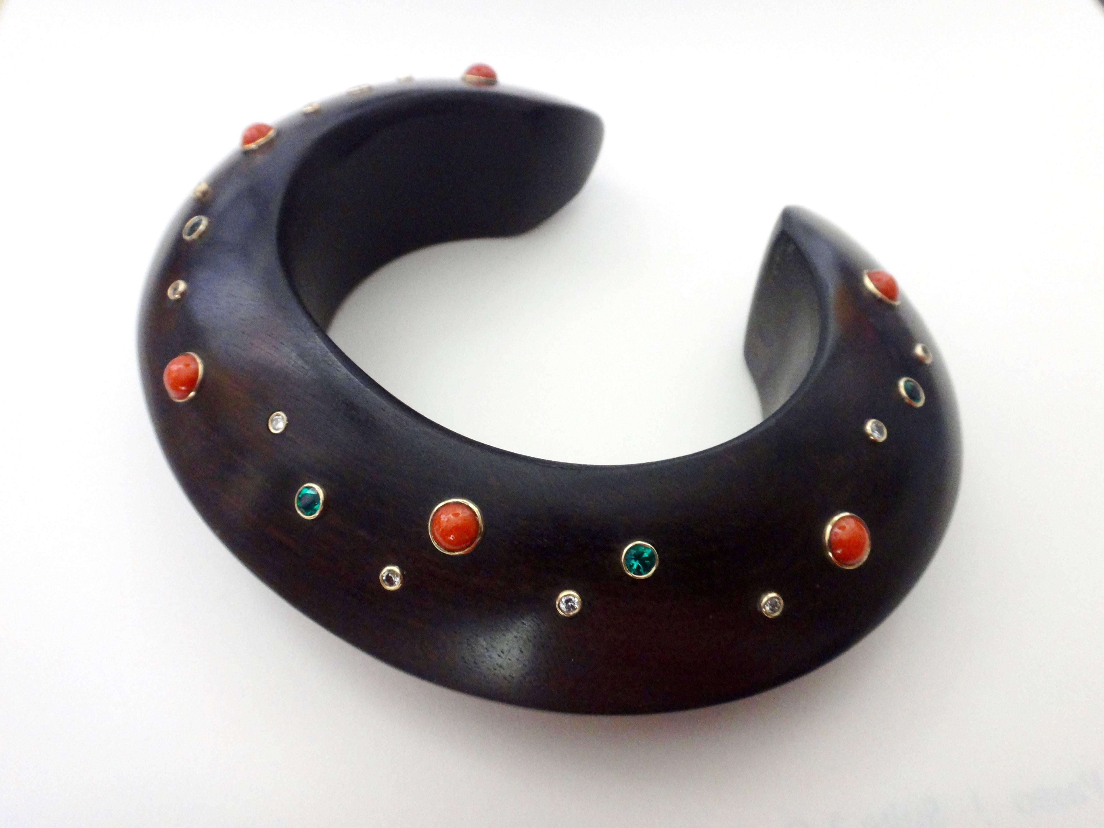 A carved ebony cuff is decorated with bezel set, faceted emeralds, Mediterranean red coral along with diamonds in this ethnically inspired bracelet.  The inside diameter of the cuff is 6 1/2 inches with an opening of 1 1/4 inches to fit an average