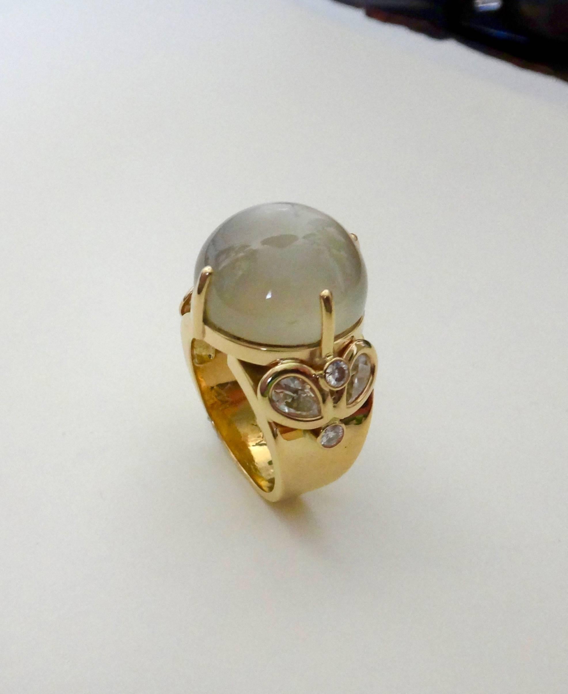 A highly domed cabochon moonstone of exceptional clarity is featured in this one-of-a-kind cocktail ring.  The center stone is flanked by a cluster of pear shaped and brilliant cut diamonds.  The handmade setting is 18k yellow gold.  The ring is a