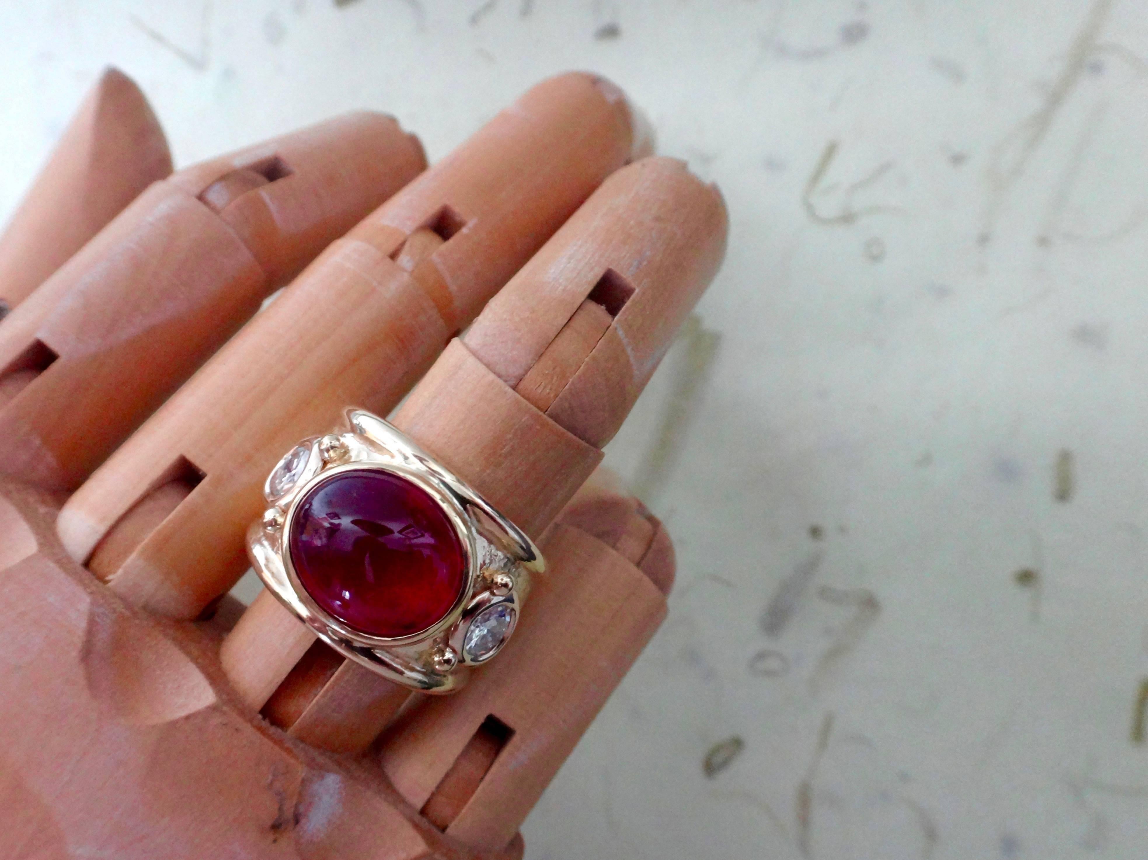 A gem quality cabochon rubelite (red tourmaline) of exceptional color and finish is flanked by a pair of brilliant cut diamonds in this "Bombe" style ring.  The three gems are bezel set in a hand fabricated, highly polished and textured