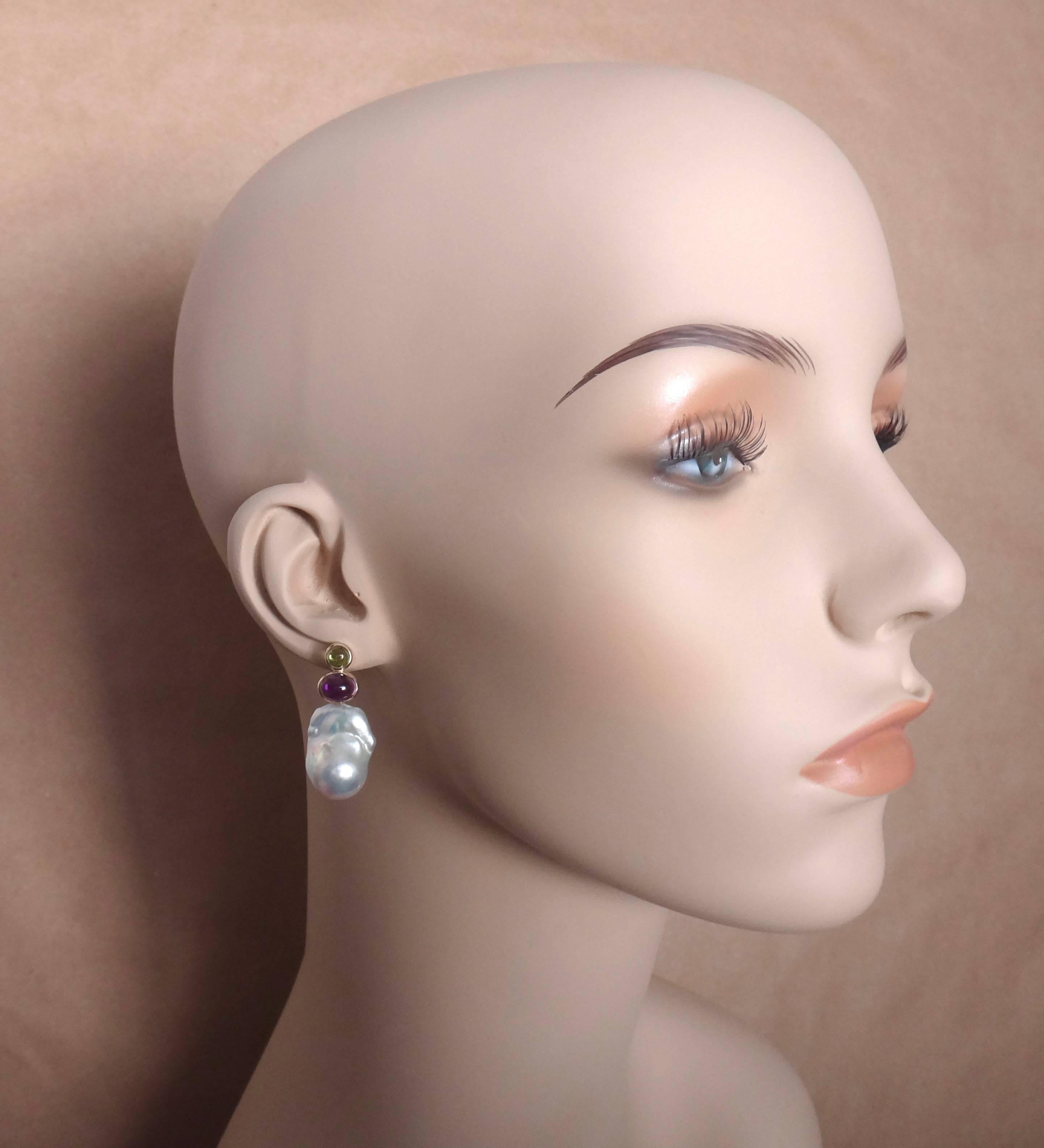 A round cabochon peridot is paired with an oval cut cabochon amethyst in these uncomplicated drop earrings.  The expertly bezel set gems intensify the whiteness of a pair of baroque cultured pearls.  The earrings have posts with jumbo friction