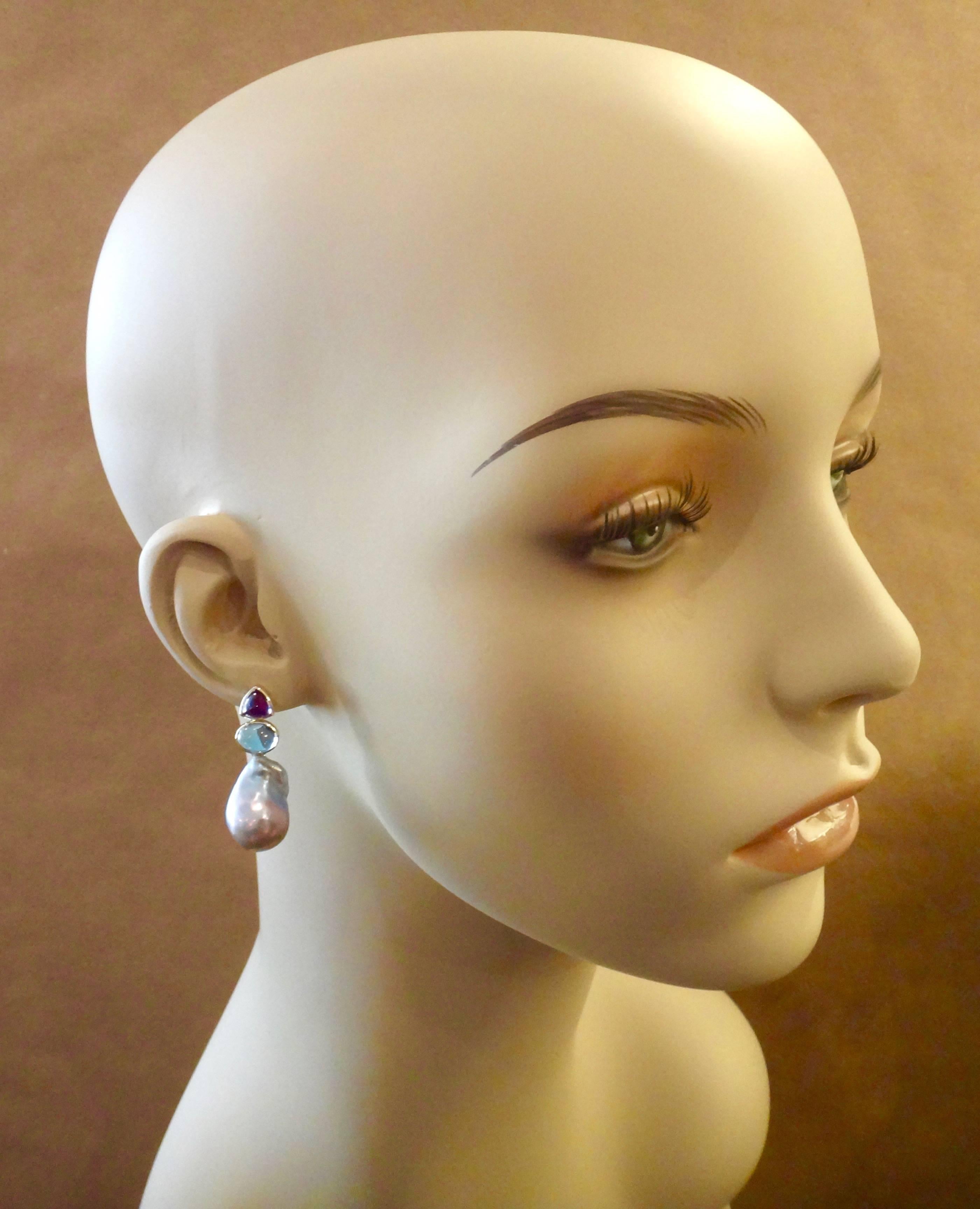 Trillion cabochon amethyst are paired with oval cut cabochon Swiss Blue topaz in these effortless drop earrings.  The expertly bezel set gems magnify the rich purple and blue colors found in a pair of baroque cultured pearls.  The earrings have