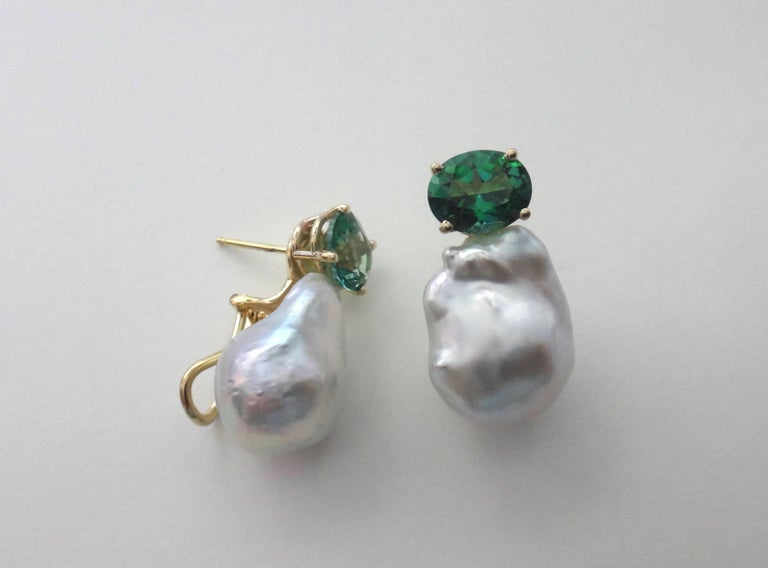 Bright and sparkling oval cut green topaz are paired with white baroque South Seas pearls in these simple and classic earrings.  Set in 18k yellow gold, the earrings have posts with omega clips for comfort and safety. 