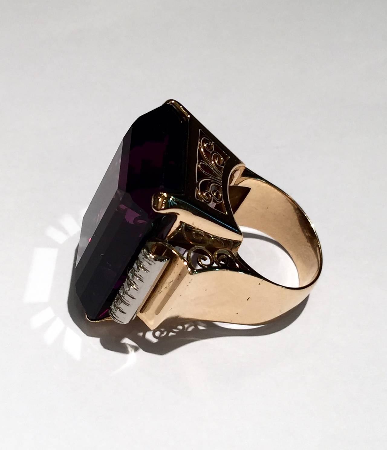 A yellow and white gold ring set in the center with a large amethyst and seven little diamonds on each side. 
1950's mounting with arabesque patterns. 
Amethyst width : 210 mm 
Weight of the stone : approximately 60 carats, in a deep purple