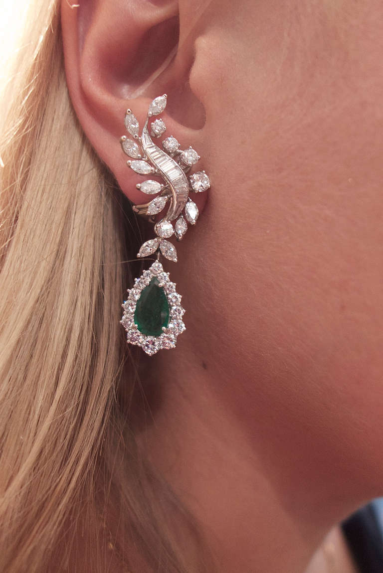 White gold and platinum earrings, the main part is set with baguette, marquise and brilliant-cut diamonds. 
A movable pear-shaped part is suspending and set with an emerald and diamonds. 
Diamonds weight: approximately 8 carats
Emeralds weight: