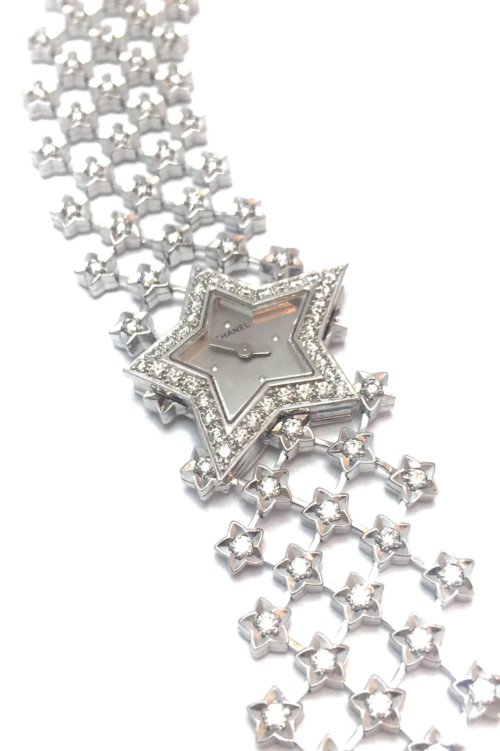 A 750/000 white gold jewelry Chanel watch, "Poussière d'étoile" collection. 
The bezel in shape of a star is set with diamonds, the large crossed motif bracelet is enhanced with falling stars, silvered dial. 
Circa 2000.
Quartz