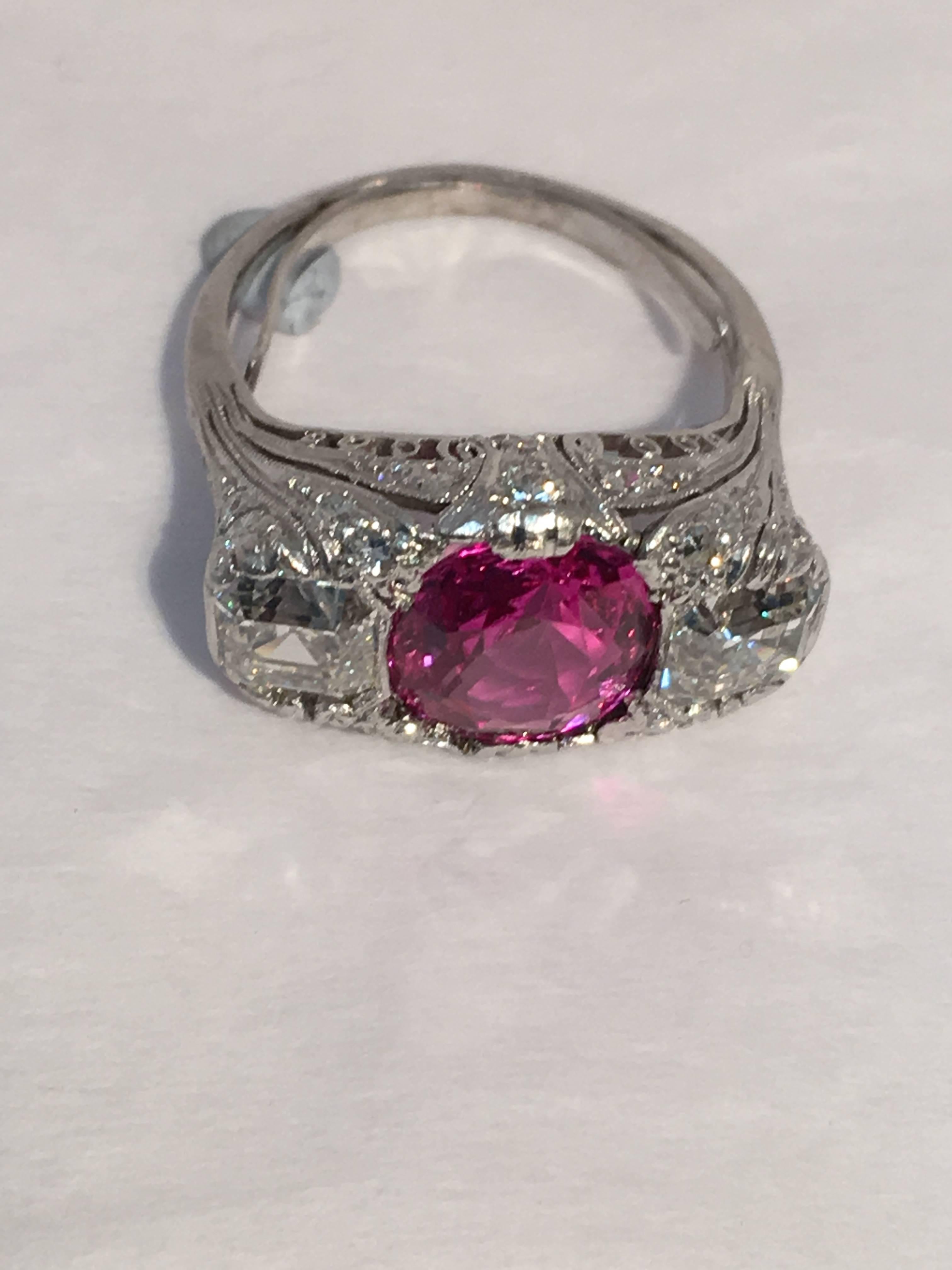 This highly detailed platinum Art Deco ring is center set with one cushion shape natural pink sapphire (GIA Sapphire Report #2121011169) weighing 3.32 carats, Type II, eye clean.  Sapphire is flanked by two Asscher cut diamonds weighing .77 cts.