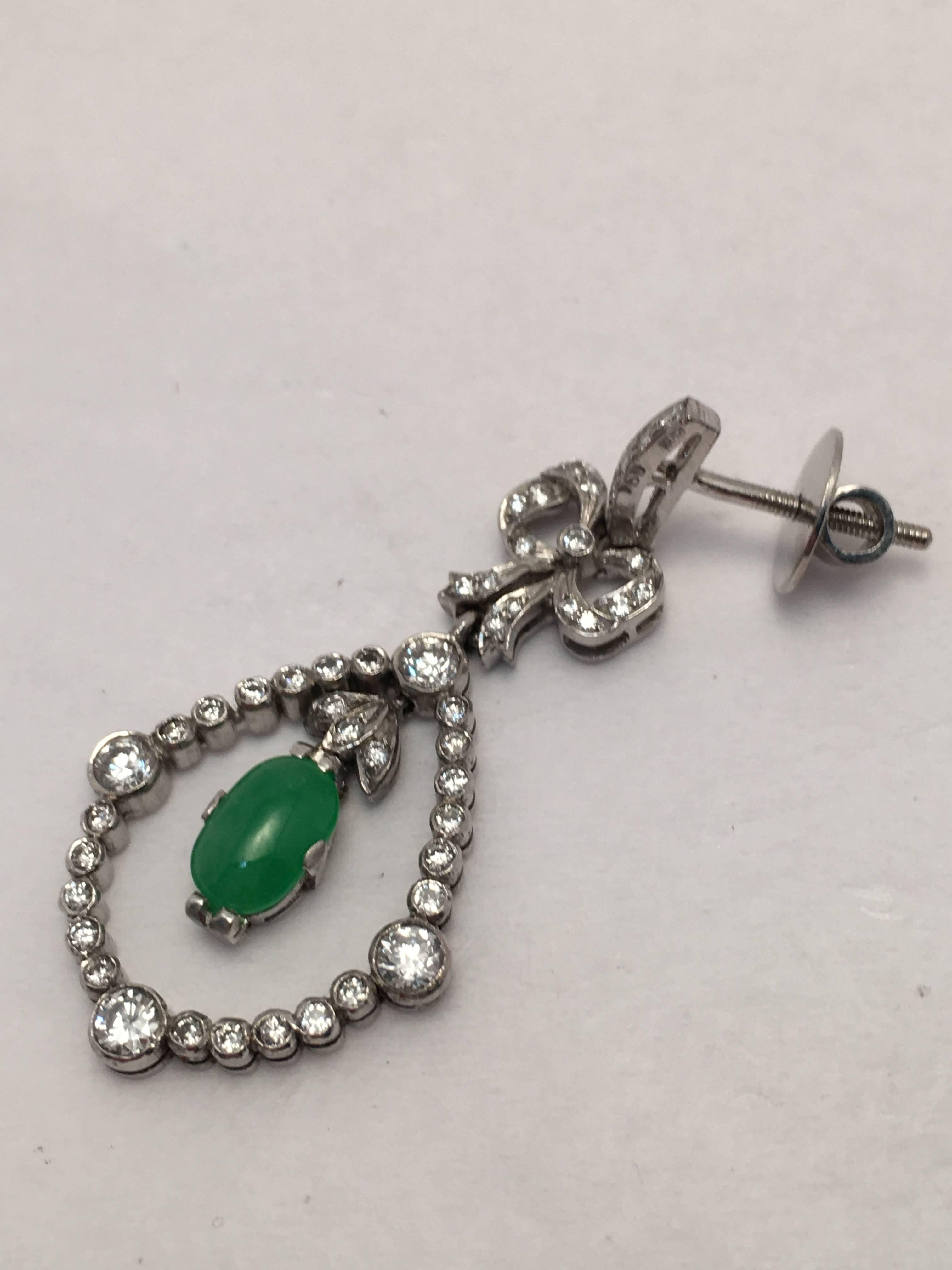 These 18 Kt. white gold drop style earrings are set with two oval dangling cabochon jade stones of very fine color.  Surrounding each jade dangle are 90 round brilliant diamonds weighing approximately 1.45 ct. total weight which hang from a