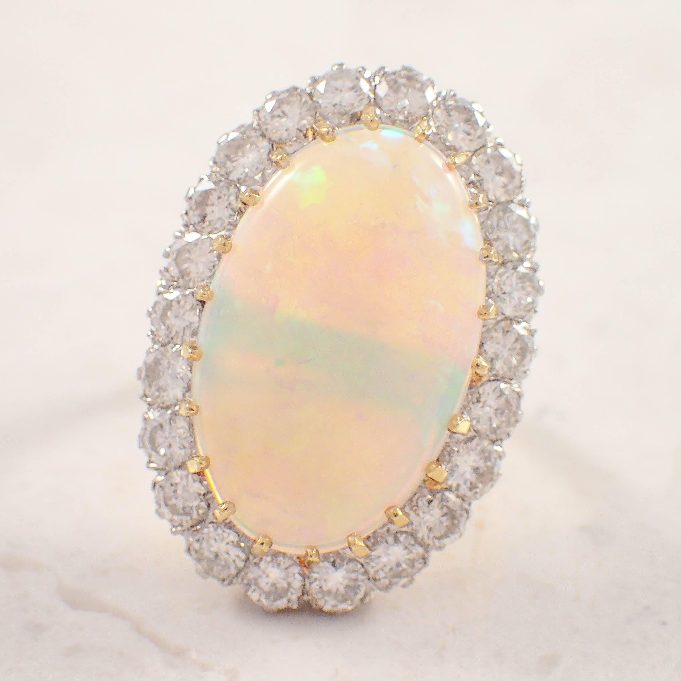 18K Yellow gold opal and diamond ring. The cluster style ring is set with one oval opal measuring 20 X 12.5 mm surrounded by 22 round diamonds weighing approximately 2.00 carats total. The ring weighs 5.1 DWTs/ 7.9 grams. Size 5.5. Circa