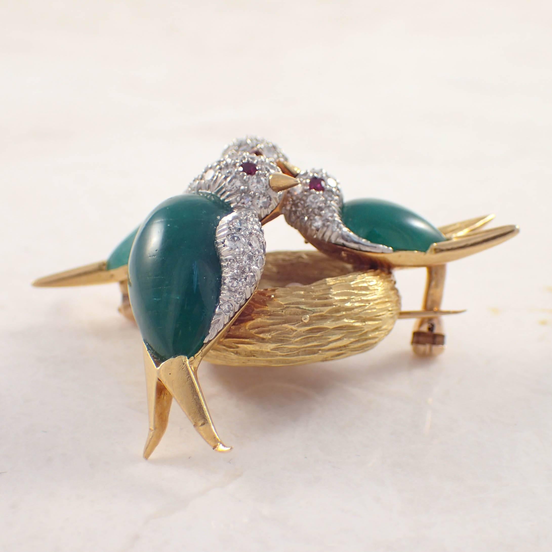 18K Yellow gold and platinum emerald, diamond and ruby bird brooch. The brooch depicts 3 birds sitting on a nest of eggs. The birds' bodies are made of 3 cabochon cut emeralds weighing approximately 17.00 carats total. The platinum bird heads are