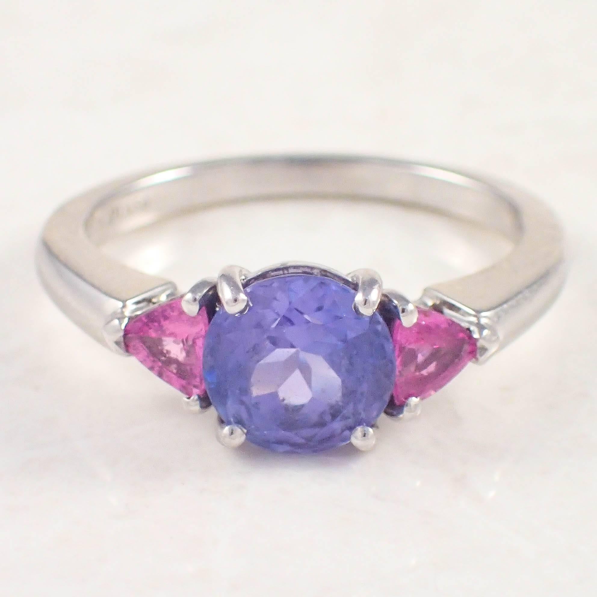 Platinum tanzanite and sapphire Tiffany & Co. ring. The three stone style ring is centered with an approximately 1.50 carat round tanzanite, accented by 2 trilliant cut, 3.5 mm pink sapphires weighing approximately .50 carat total. Stamped 