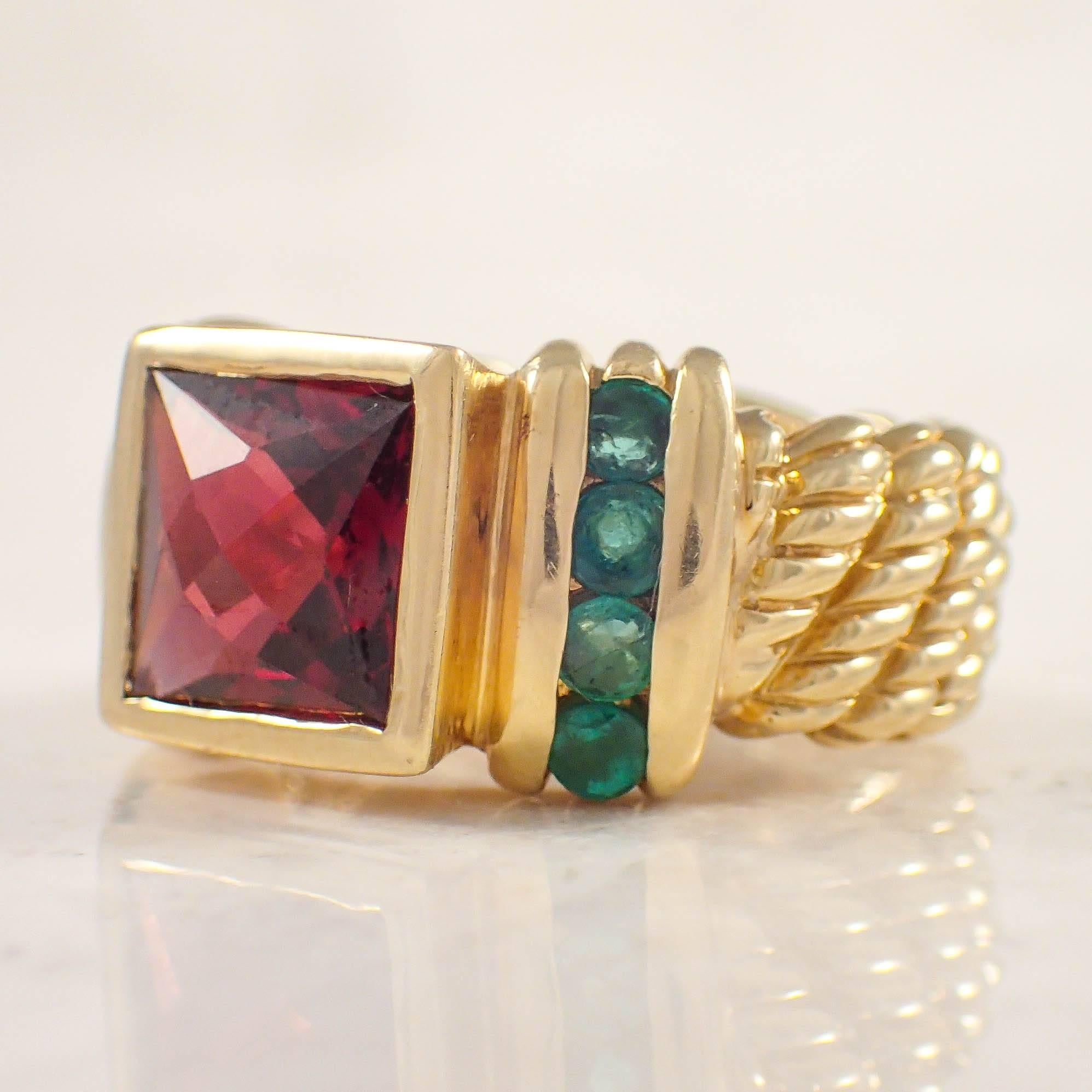 18K Yellow gold David Yurman garnet and emerald ring.  The twisted wire ring is bezel set with 1 square garnet measuring 10 mm, accented by 8 round emeralds. The ring weighs 11.9 grams. 
Stamped 