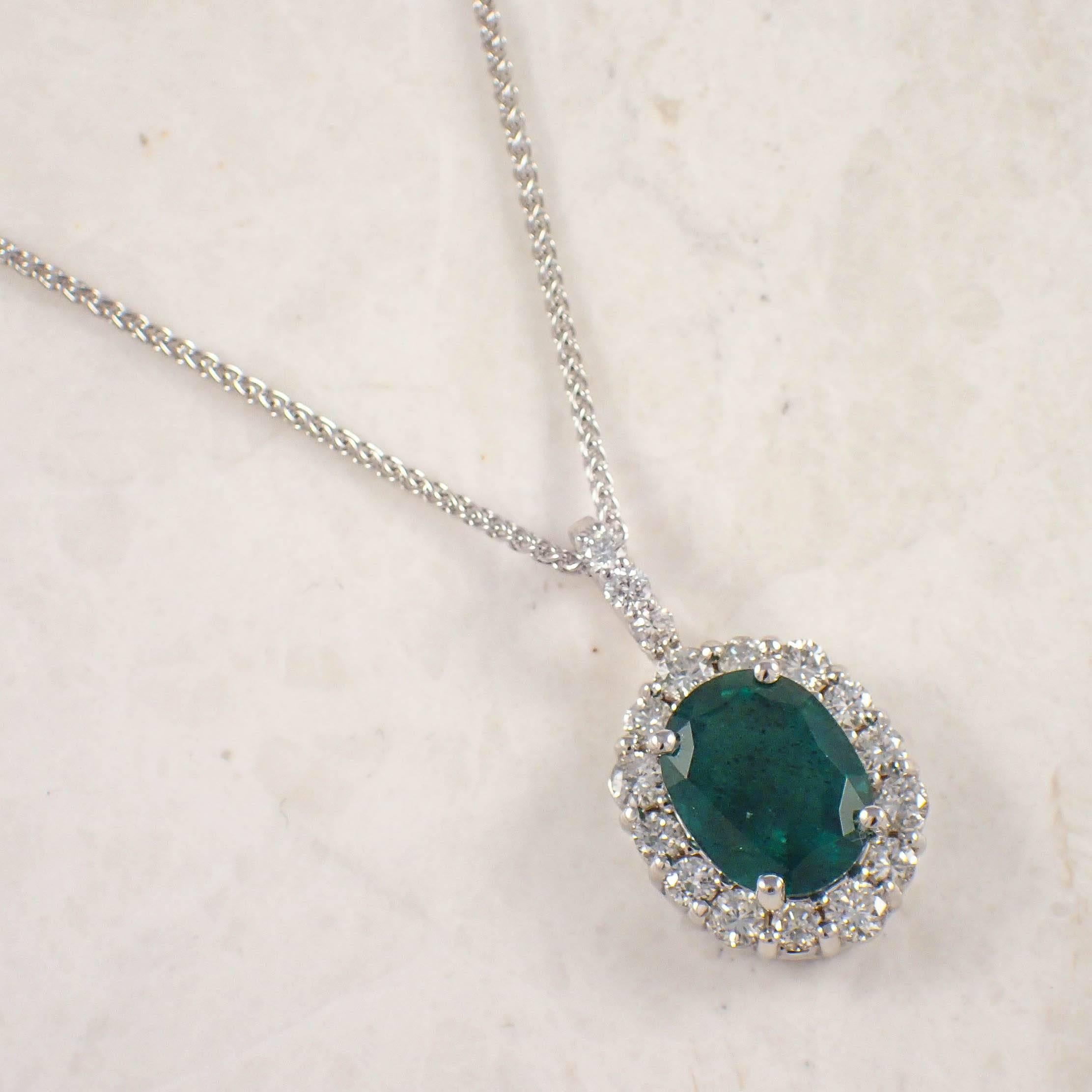14K White gold emerald and diamond pendant. The cluster style pendant is prong set with an approximately 3.20 carat oval emerald measuring 11.3 X 8.7 mm, surrounded by 17 round diamonds weighing approximately 1.00 carat total. The pendant is