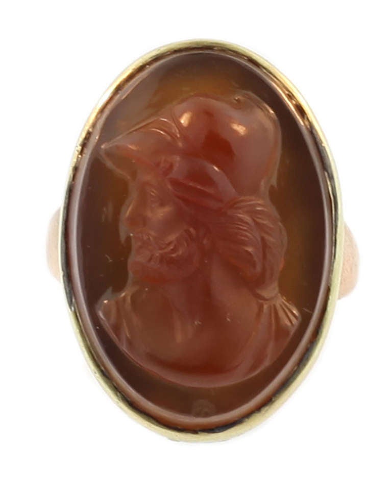 This ring is set in 14 KT yellow gold which has been tested. It is antique circa 1890. The central plaque depicts a detailed roman centurion carved in deep honey coloured agate. The ring measures size 9.25 and is in good condition.