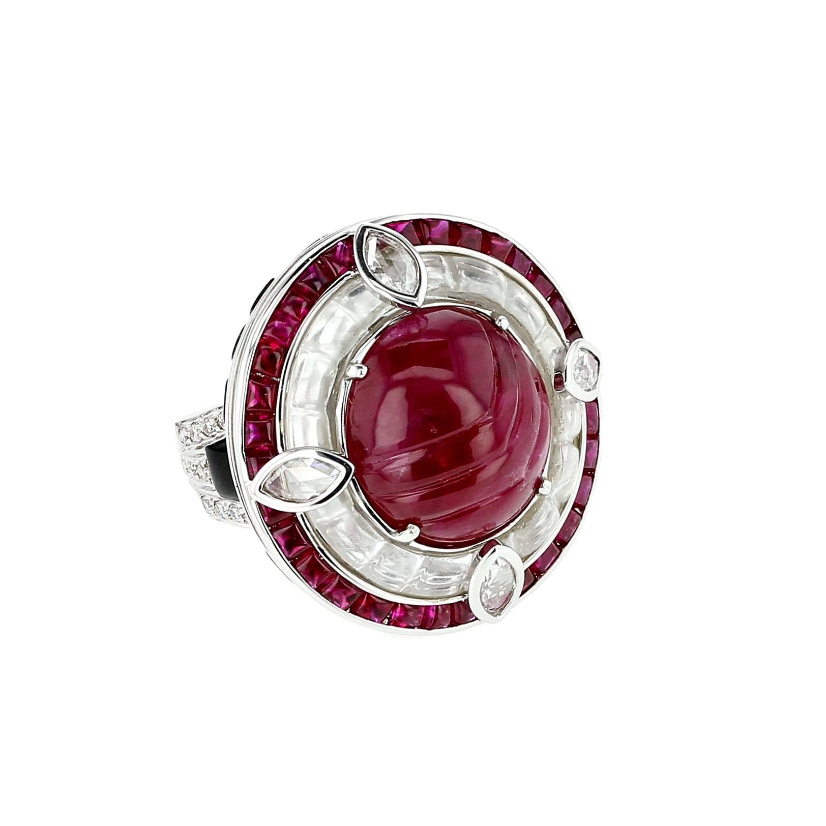 A bold and beautiful cocktail ring centered with a large near-round carved ruby weighing an estimated 17.61 carats, clustered with concentric rings of channel-set rectangular shape rock crystal and princess cut rubies, flanked by tapered geometric