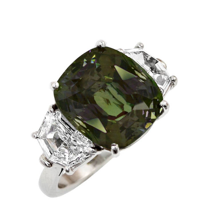 A magnificent and impressive eleven-carat cushion-shape genuine and natural Alexandrite flanked with two shield step-cut diamonds, set in Platinum. The Alexandrite originates from Sri Lanka (Ceylon), exhibits strong color-change in daylight to warm