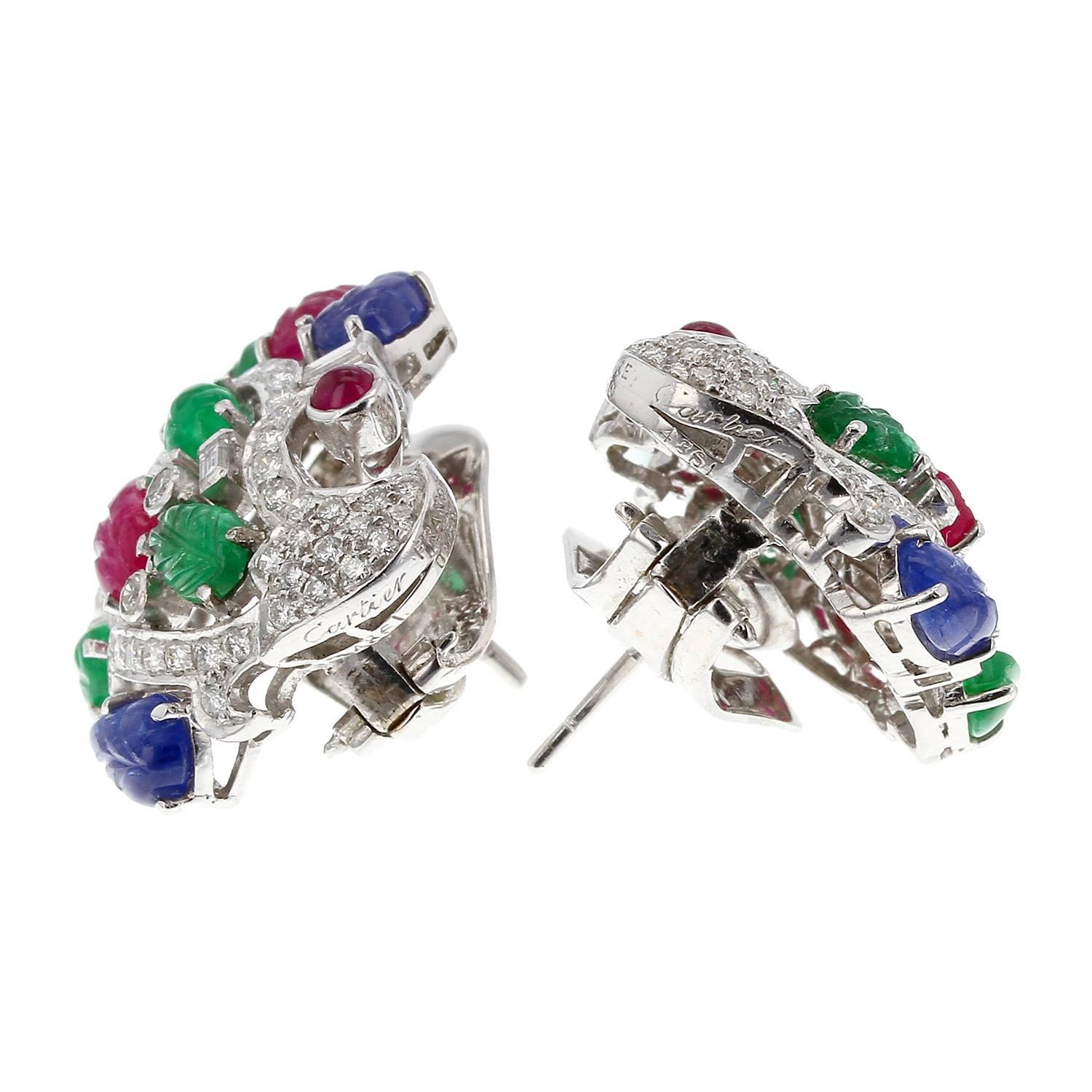 An extremely rare and magnificent Tutti Frutti earrings by Cartier, France. The post and clip-on earrings exhibit a floral design set with carved emeralds, sapphires, rubies, accented with full, single, and baguette-cut diamonds; each signed and