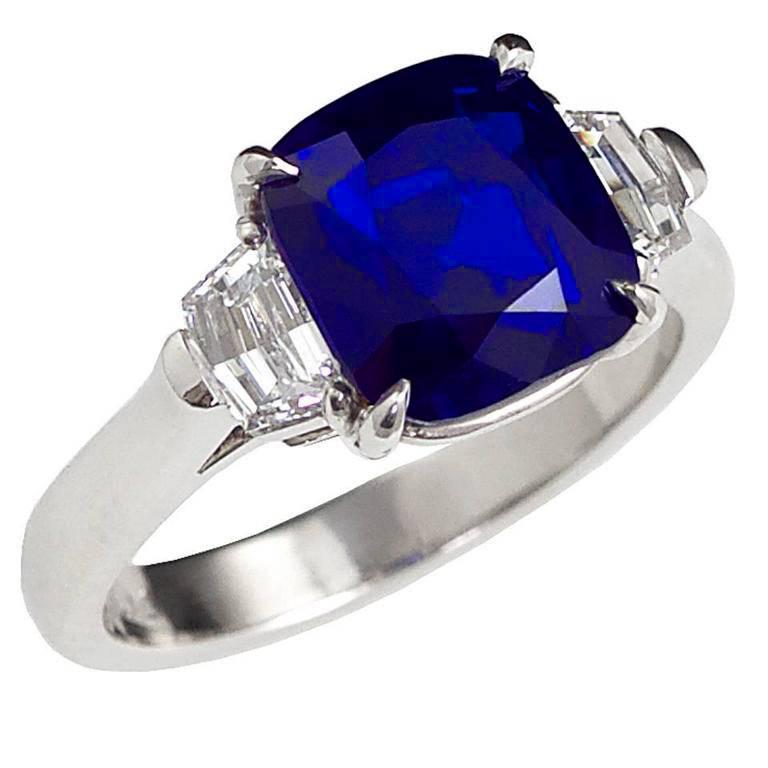 A beautiful and deep blue cushion shape Kashmir sapphire weighing over four carats, accented with two step-cut diamonds in a classic three-stone setting, made in Platinum, ring size 6 1/2 US. The sapphire accompanies a gemological report from AGL