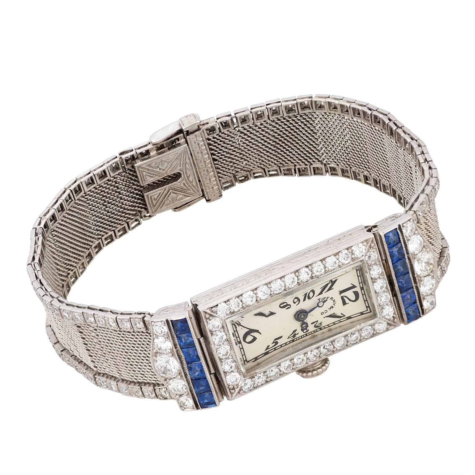 An Art Deco Tiffany & Co. diamond and sapphire platinum watch.  The watch has a beautiful hand engraved platinum case, encrusted with diamonds and sapphires, and a mesh platinum bracelet lined on both sides with diamonds.  The watch contains a